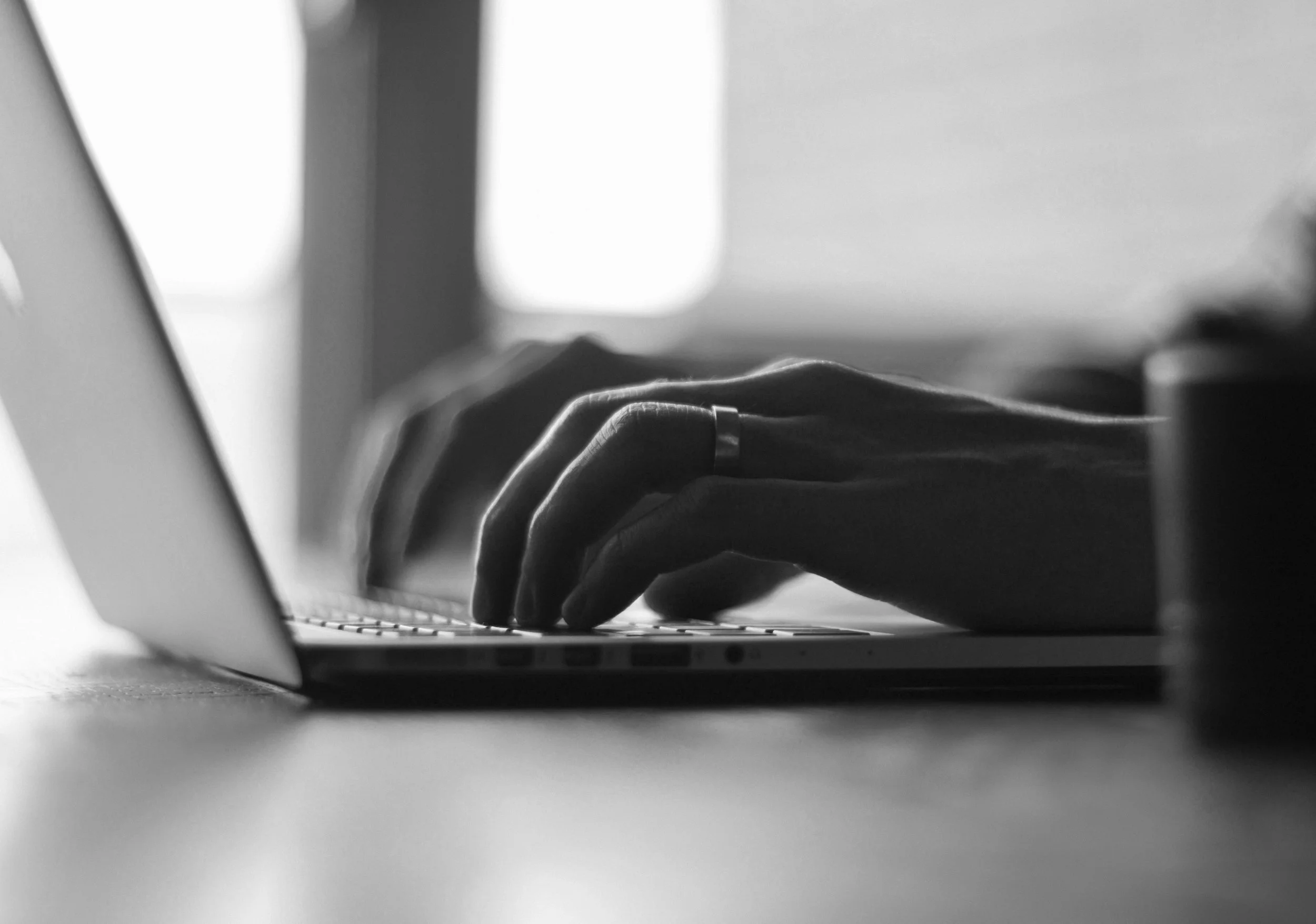 Close-up of person's hand typing on a laptop keyboard, black and white photo.