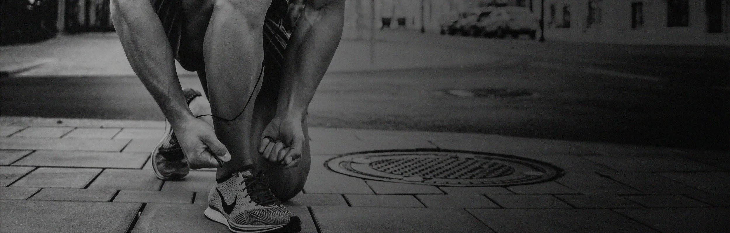 A person tying their running shoe on a city sidewalk at night.