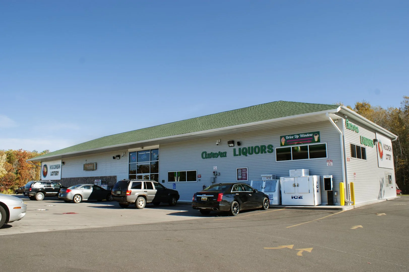 Exterior view of Aurora Liquors, a liquor store, with cars parked in the lot and a blue sky above.