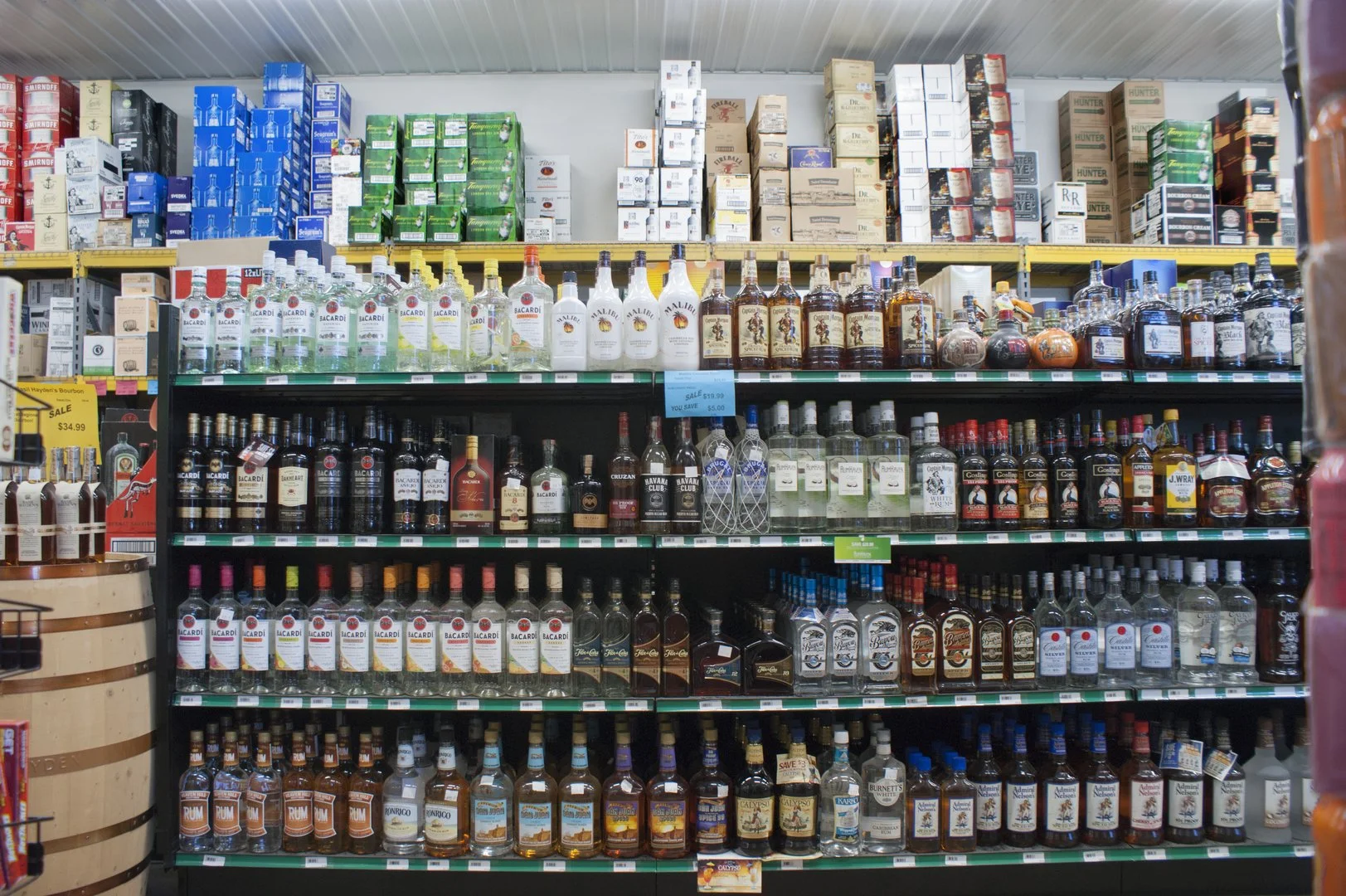 Shelves stocked with various bottles of alcohol, including vodka, whiskey, rum, and mixers, in a grocery store.