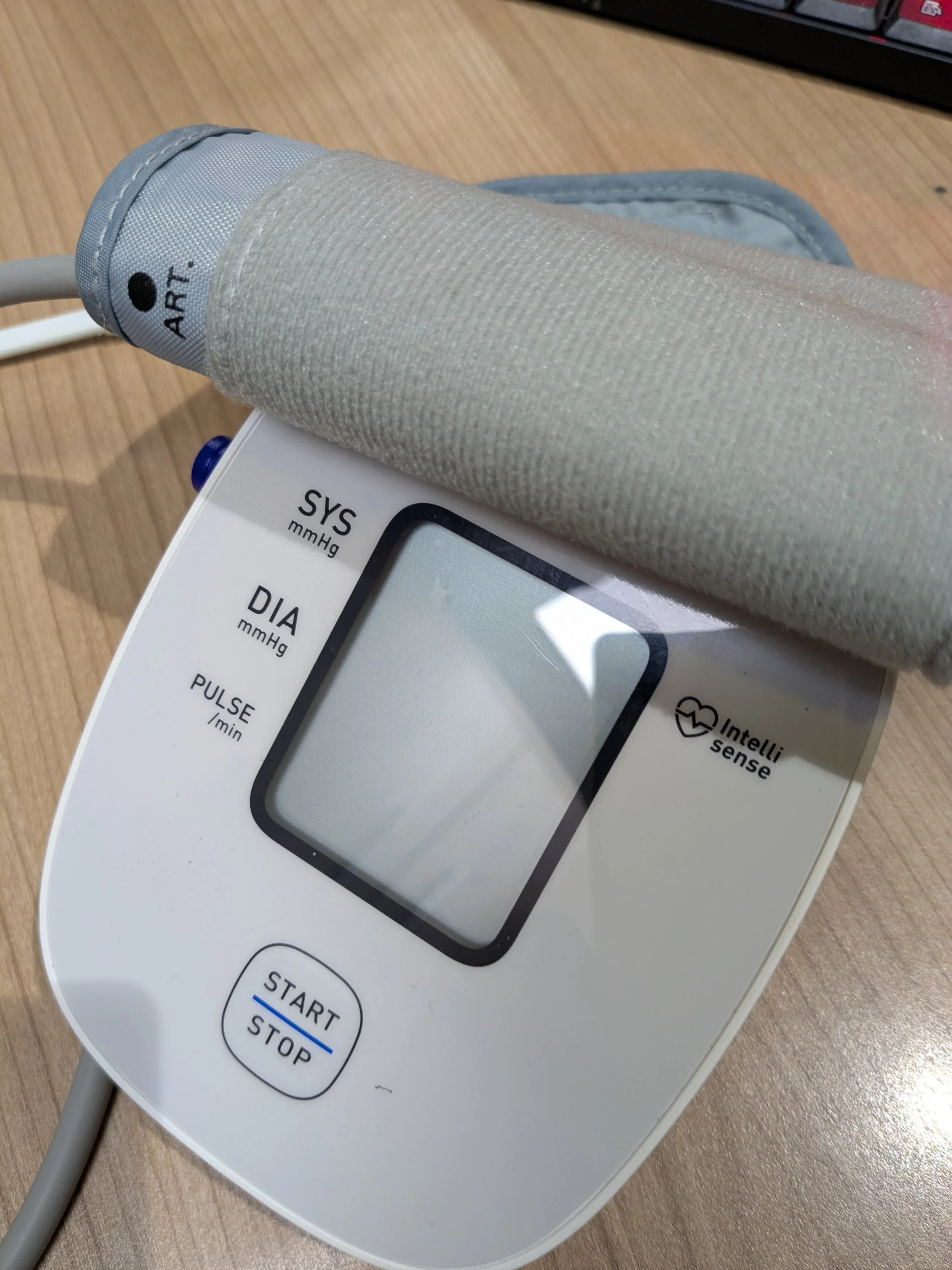 A digital blood pressure monitor on a wooden surface with the cuff wrapped around the upper part of the device.