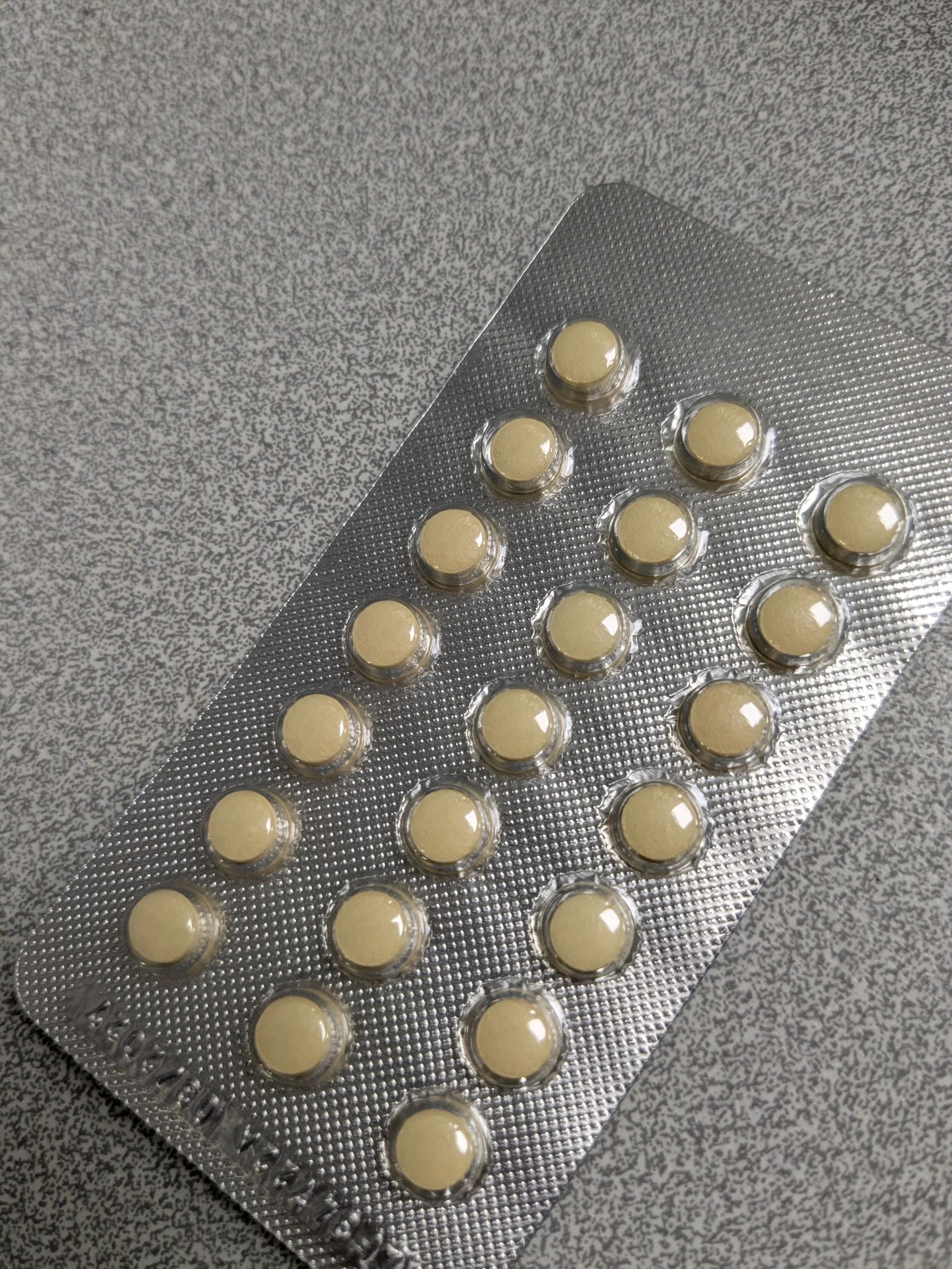 Blister pack of cream-colored pills on a speckled gray surface.