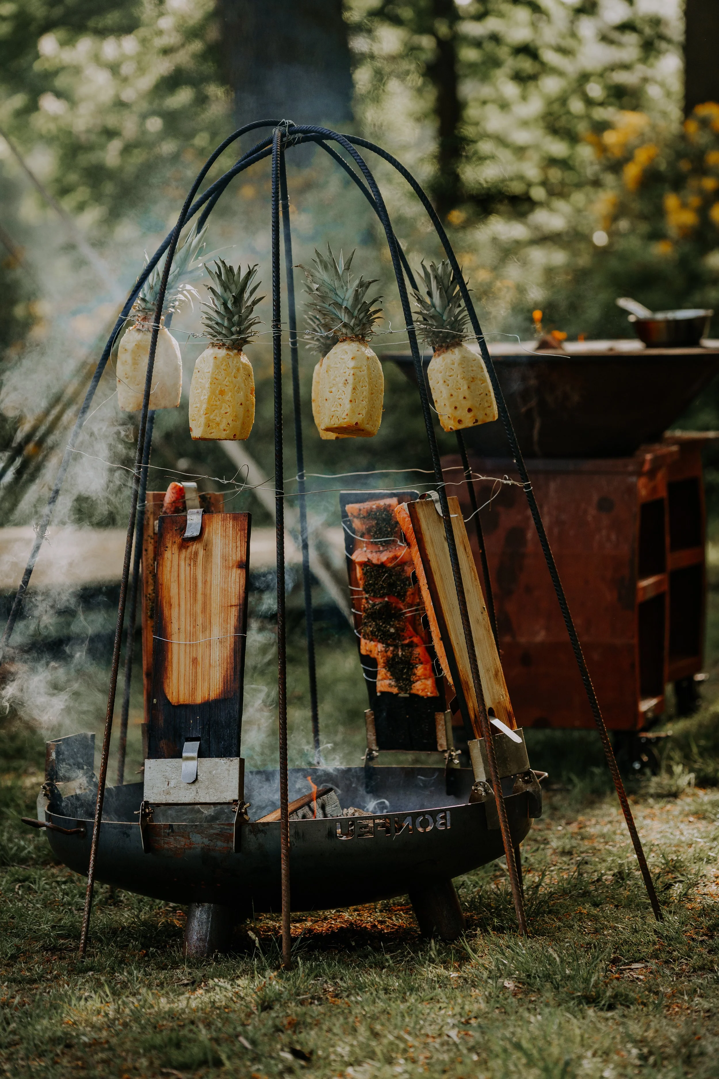 Pineapple slices and pieces of salmon being grilled over an outdoor fire pit.