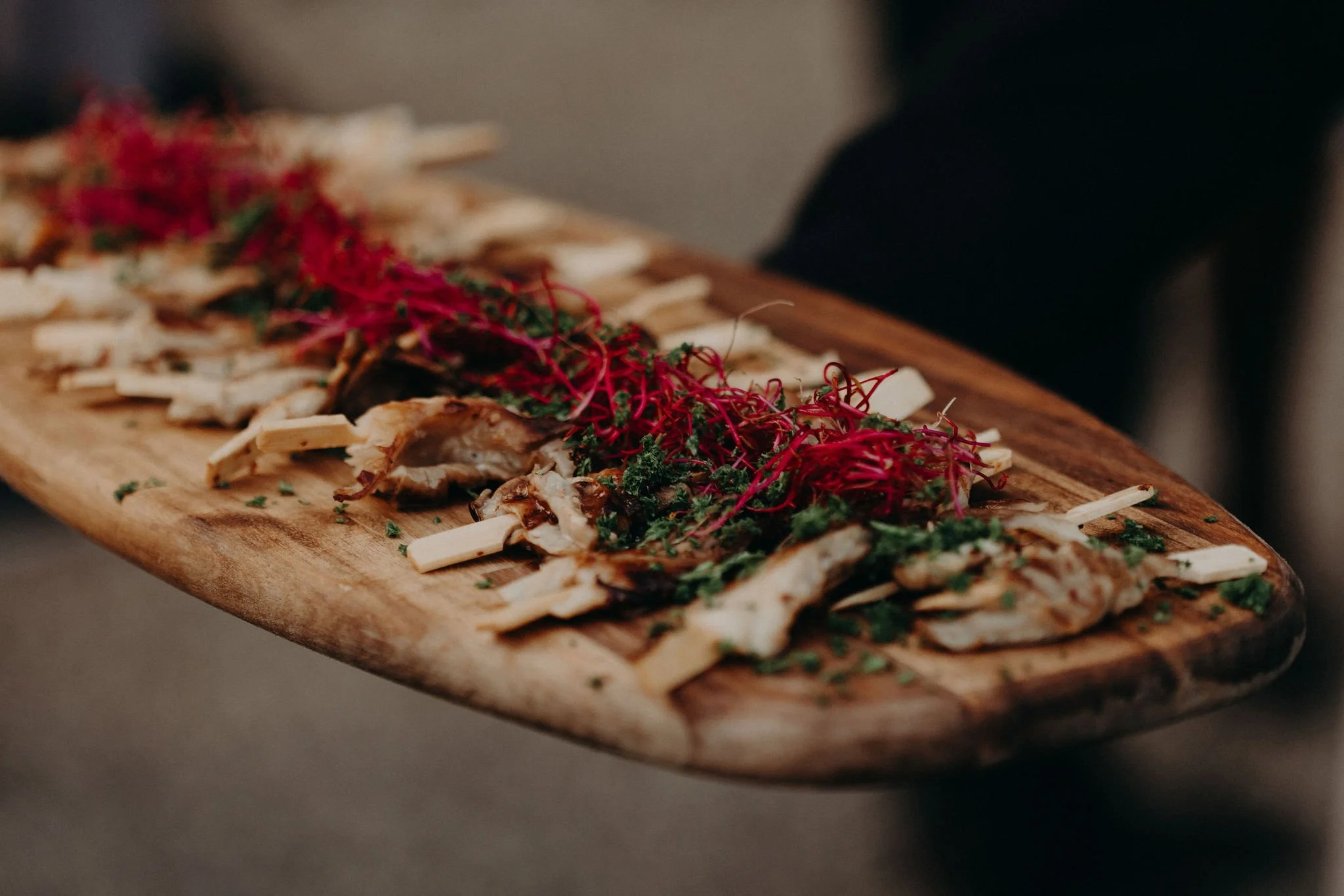 A wooden serving platter with slices of grilled chicken garnished with microgreens and topped with bright red edible flowers