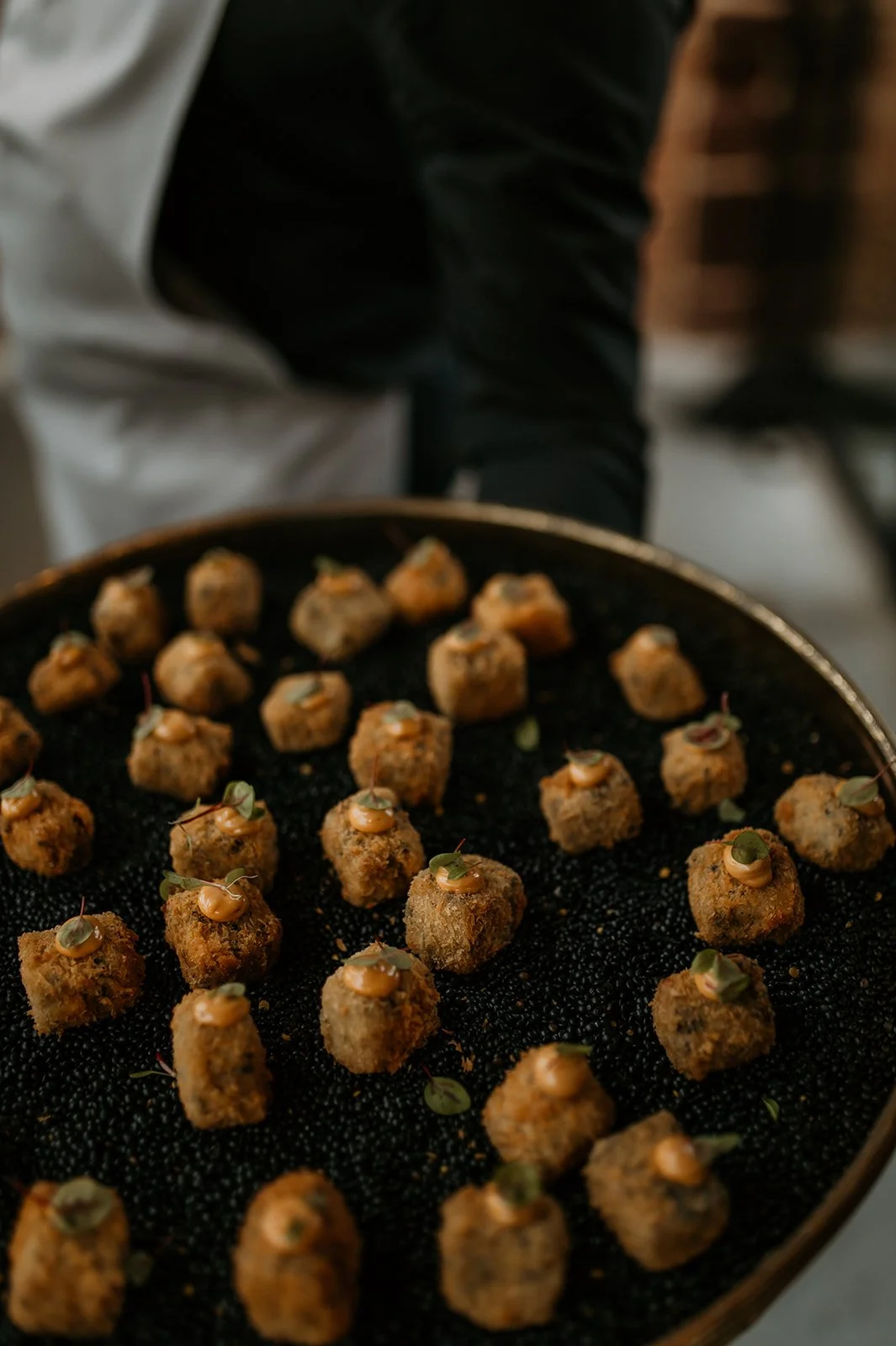 A tray of breaded bites garnished with green herbs and a creamy orange sauce.