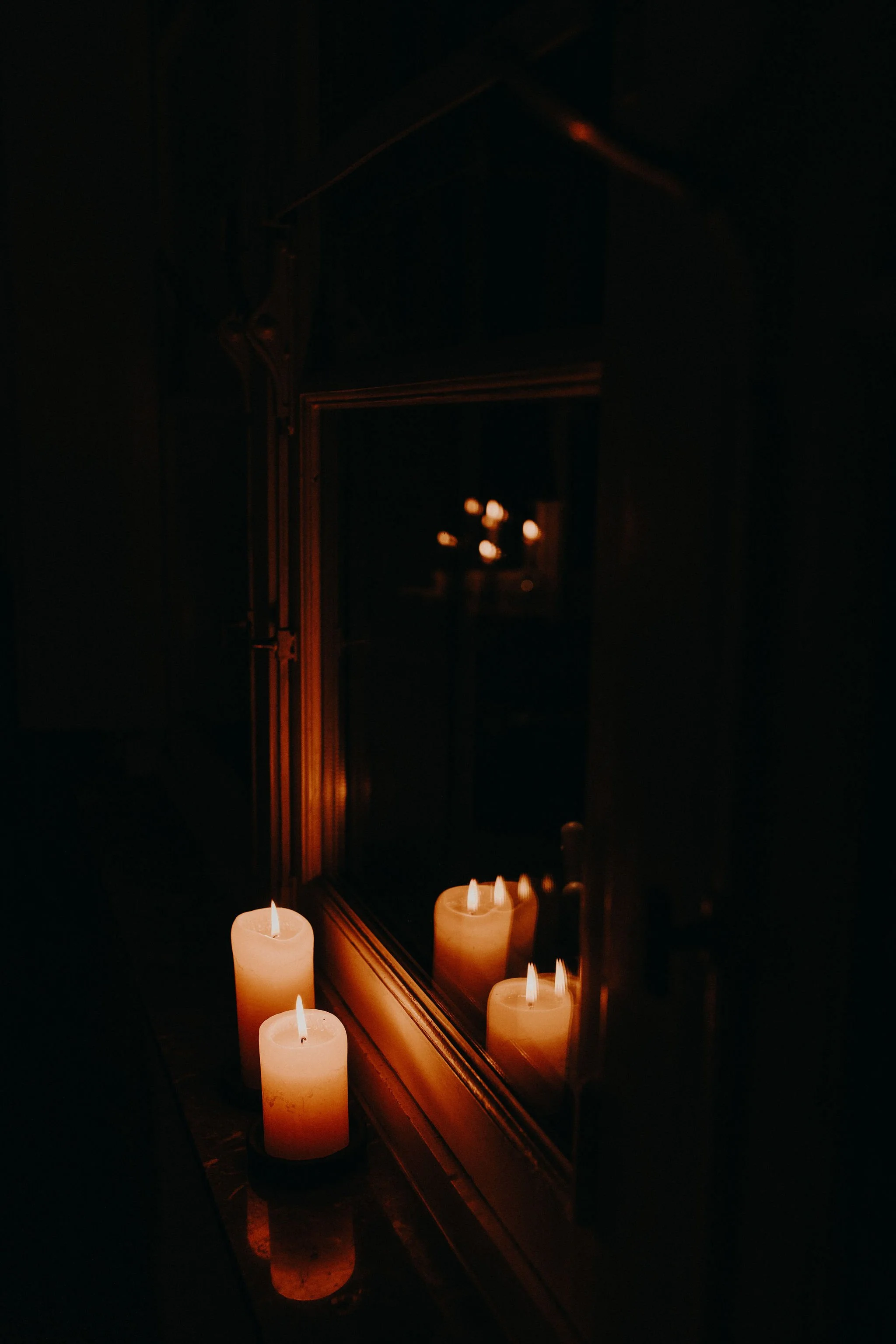 Three lit candles placed on a surface near a mirror, creating a warm glow in a dark room.