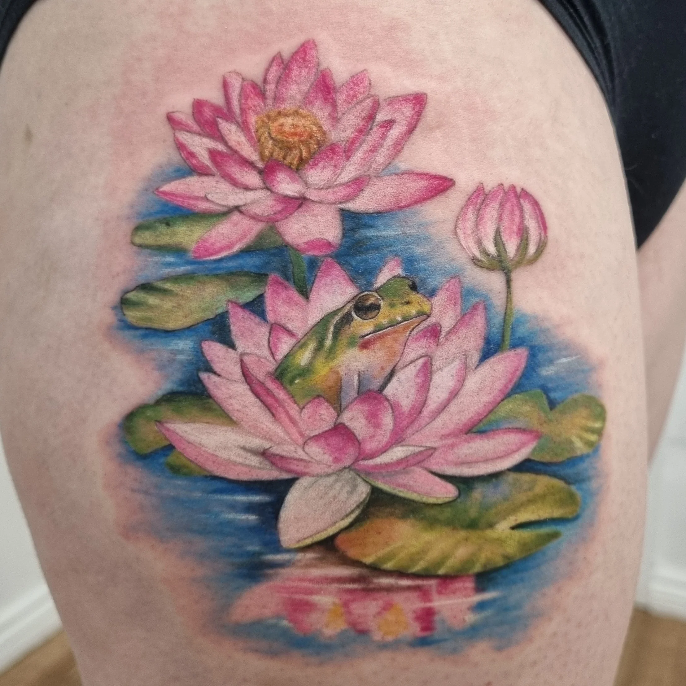 Colour realism tattoo of a frog sat in a water lily.