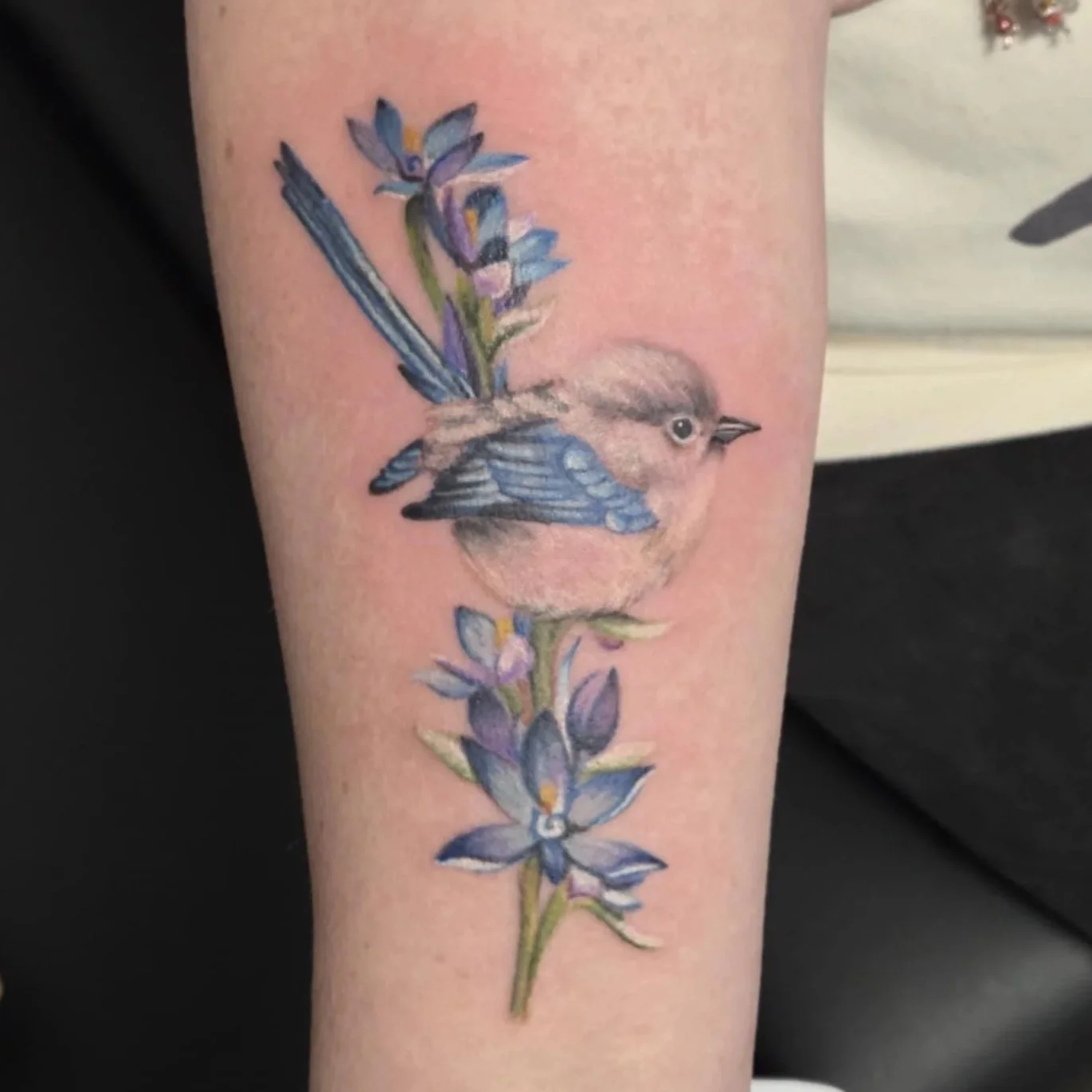 Tattoo of a small wren with blue and purple flowers