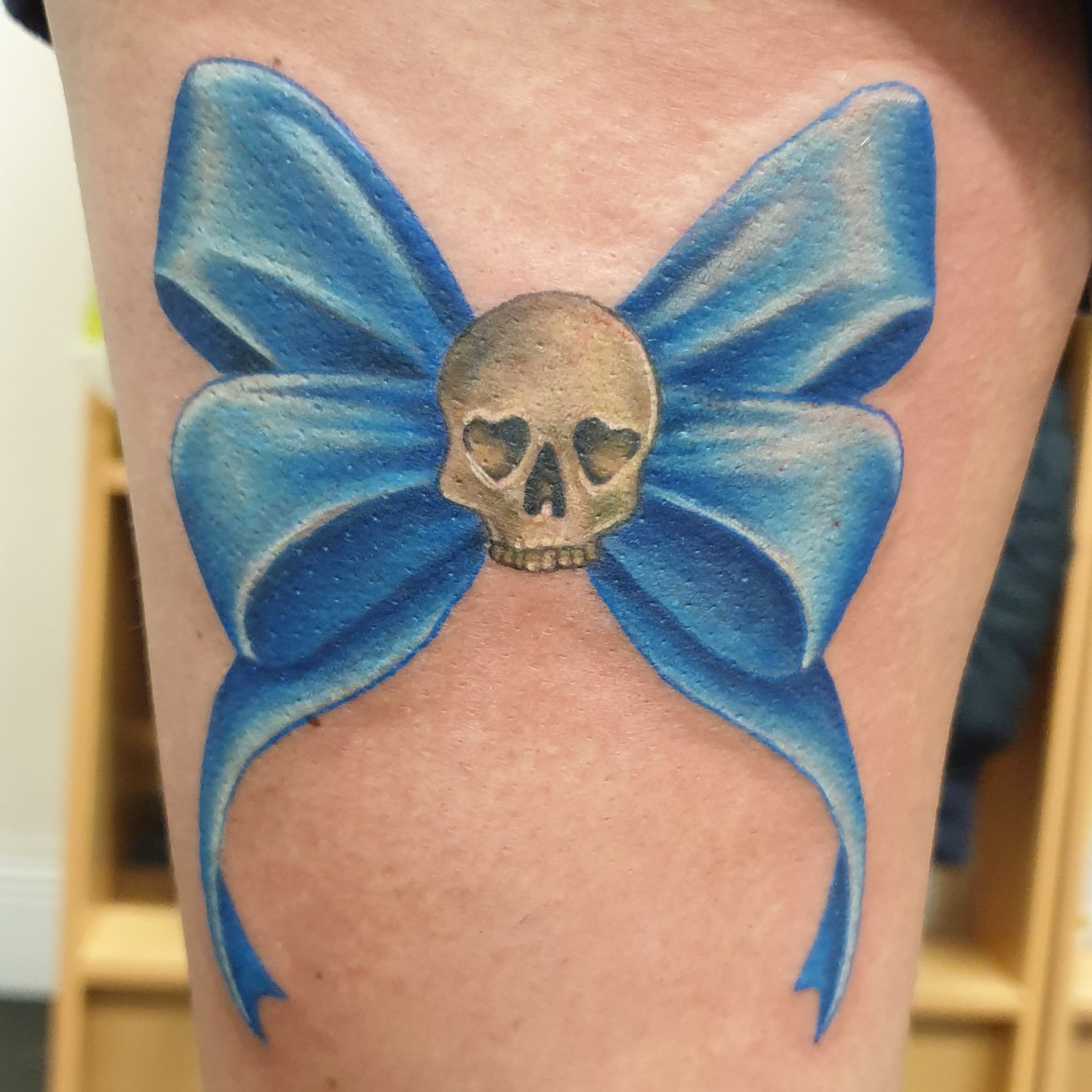 A colour tattoo of a blue ribbon bow with a small skull in the centre