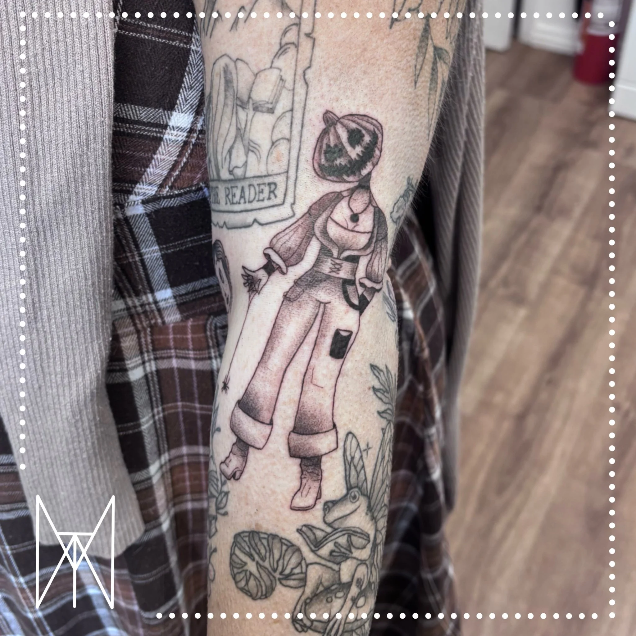 A black and grey tattoo of a scarecrow with a pumpkin head