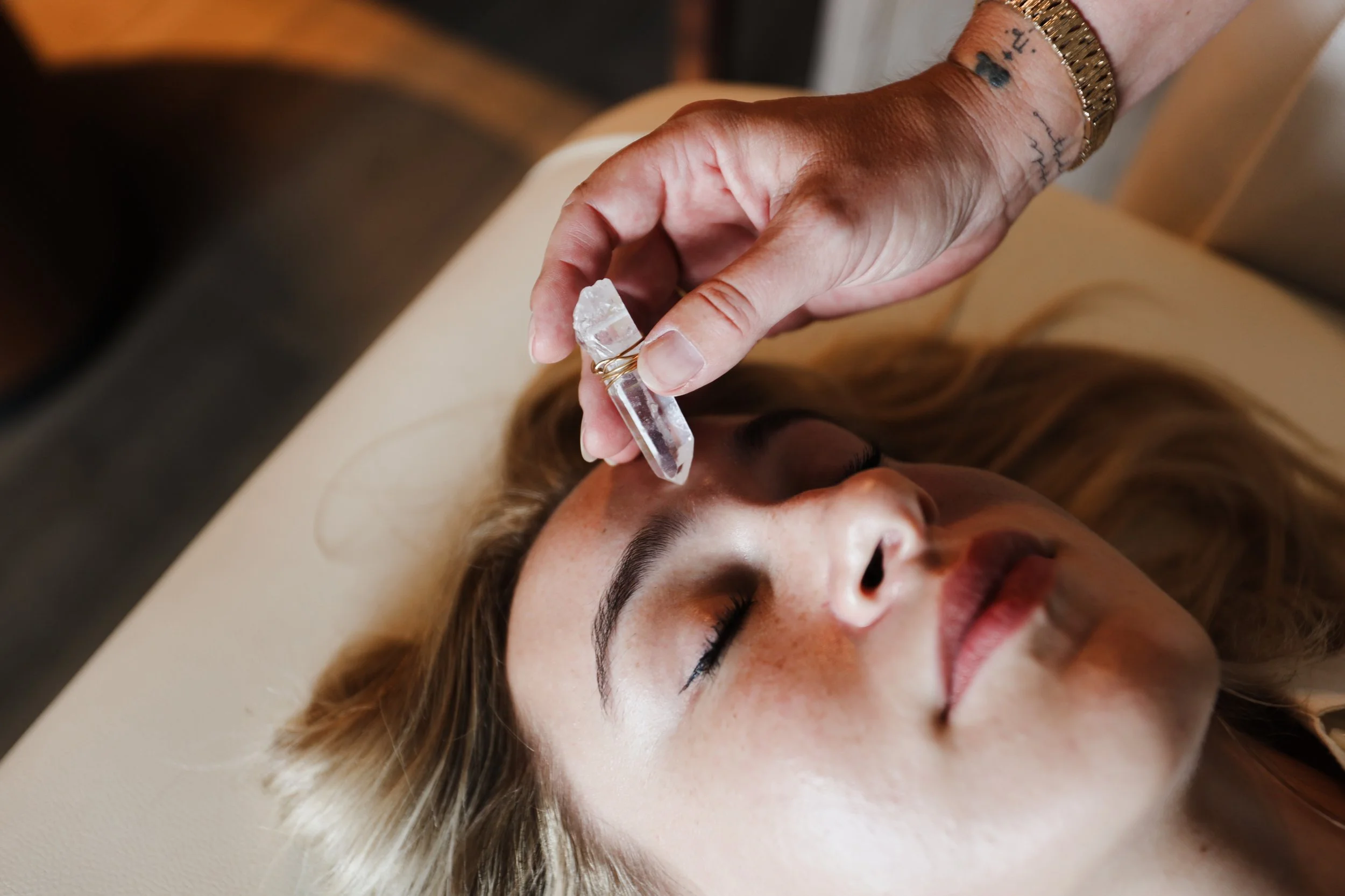 A woman with light skin and blonde hair receives a crystal needle facial treatment while lying on a beige treatment bed with her eyes closed.