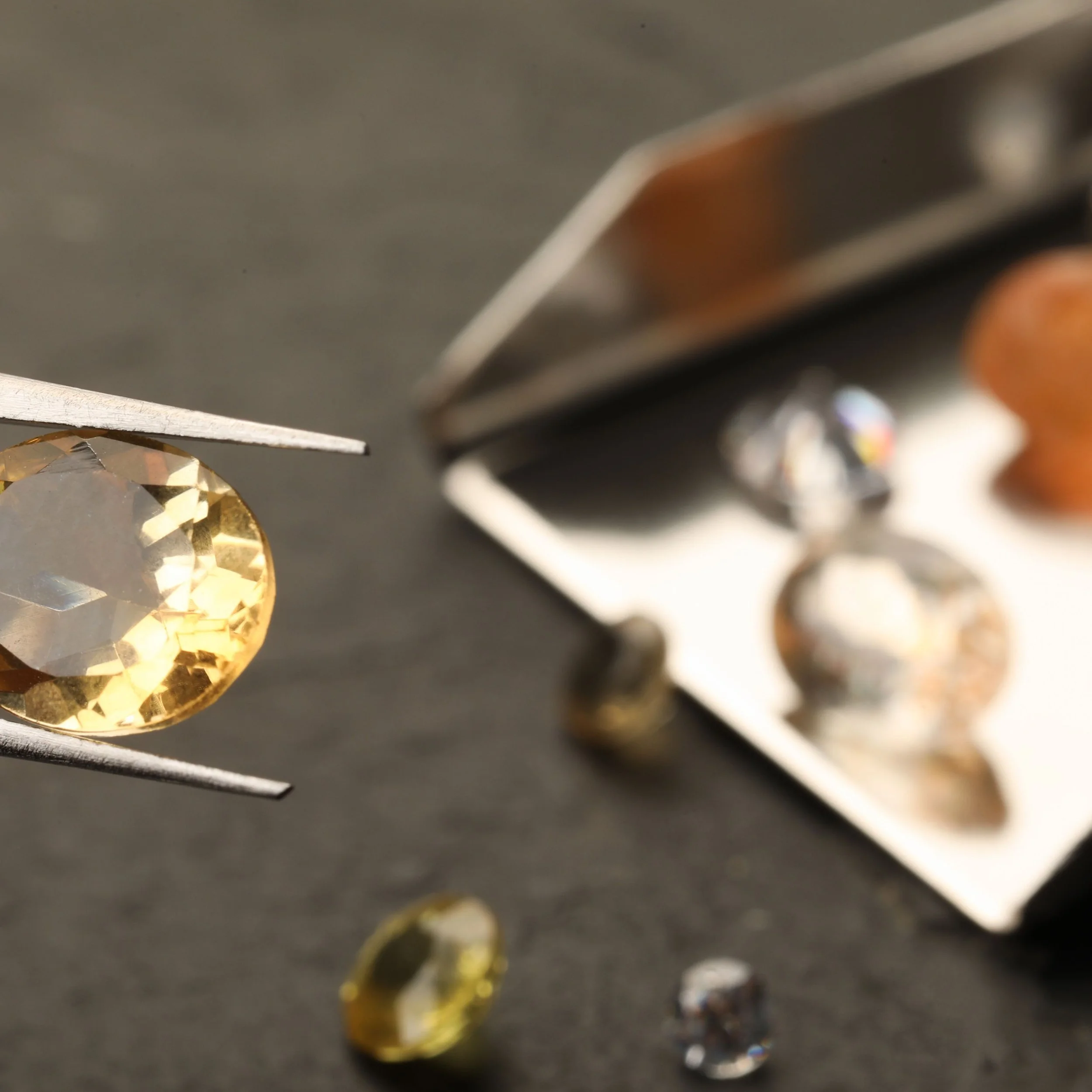 A plastic organizer containing various colored small glass or acrylic gemstones, including purple, blue, pink, yellow, and green, with sunlight creating reflections and bokeh effects.