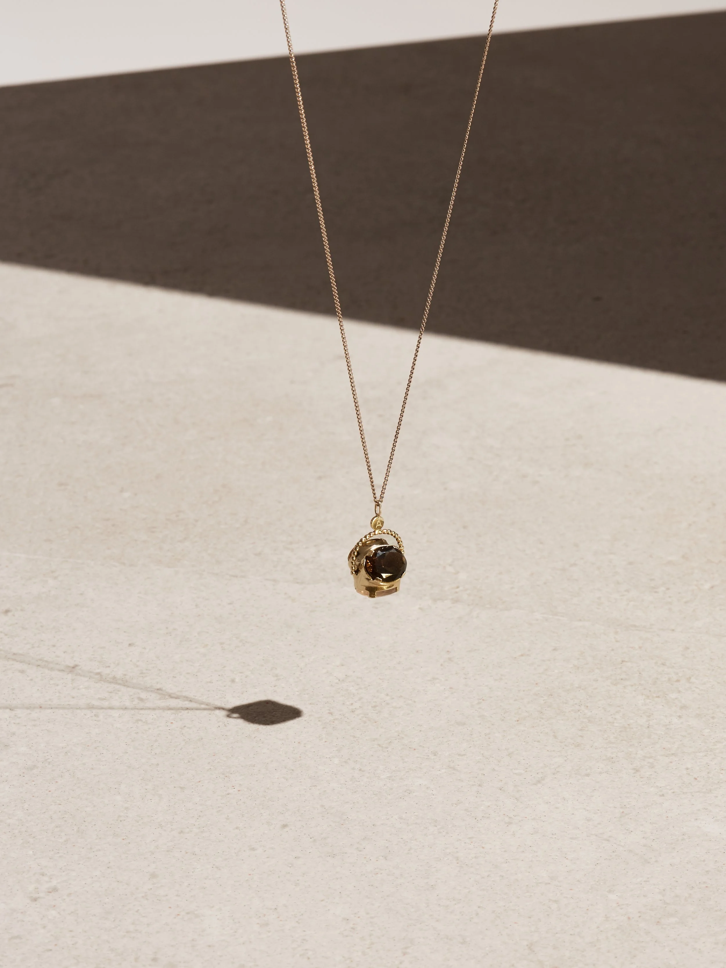Gold necklace with a dark gemstone pendant hanging against a light background, casting a shadow.