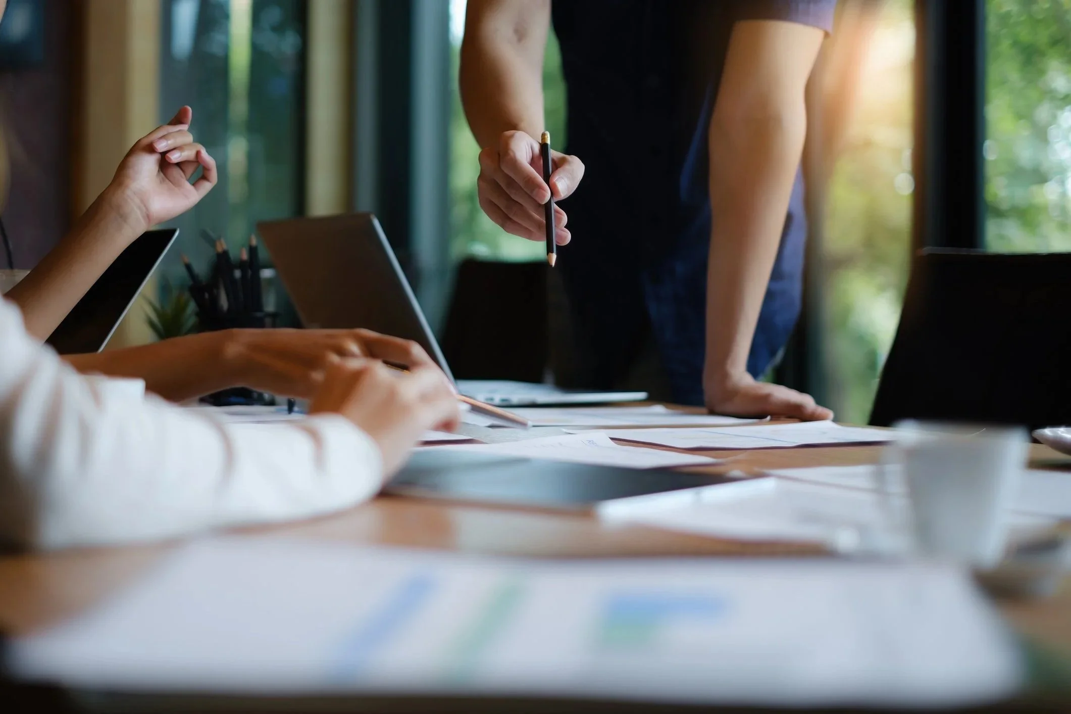 People working on a table with laptops and documents, someone standing and pointing with a pen, during a collaborative meeting working on strategy, branding, creative, digital marketing.