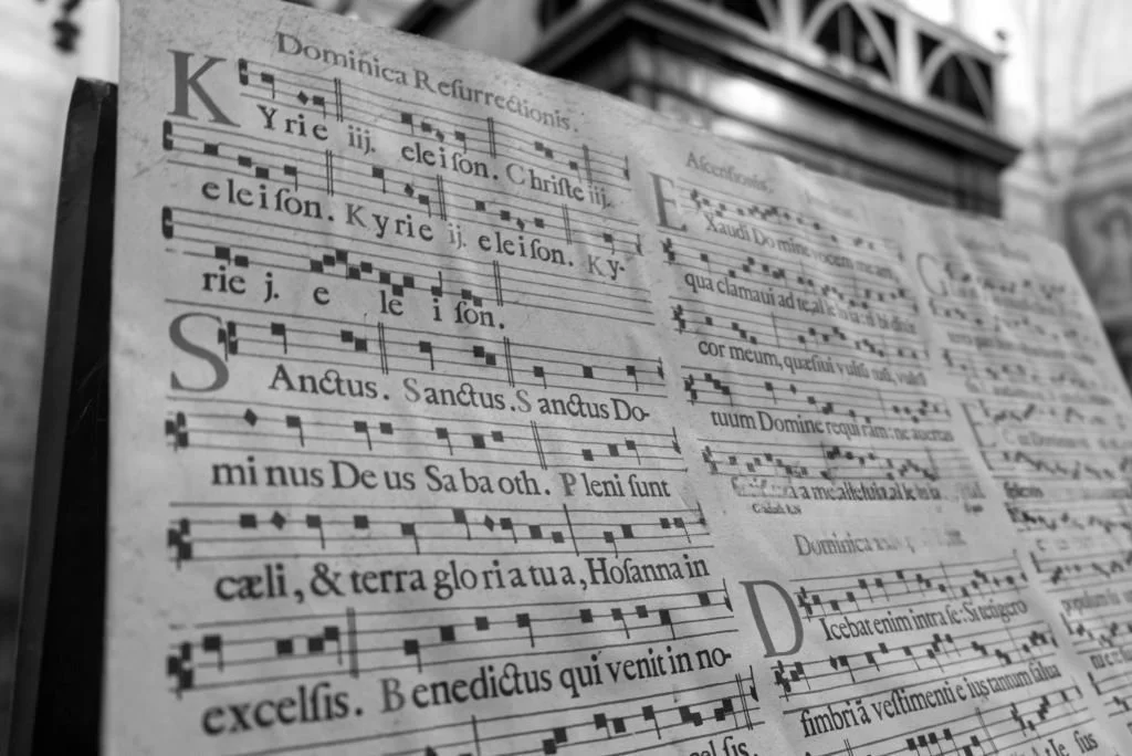Close up of book of printed choral chant music, with lyrics in Latin and simple notation, on display inside a gothic church.