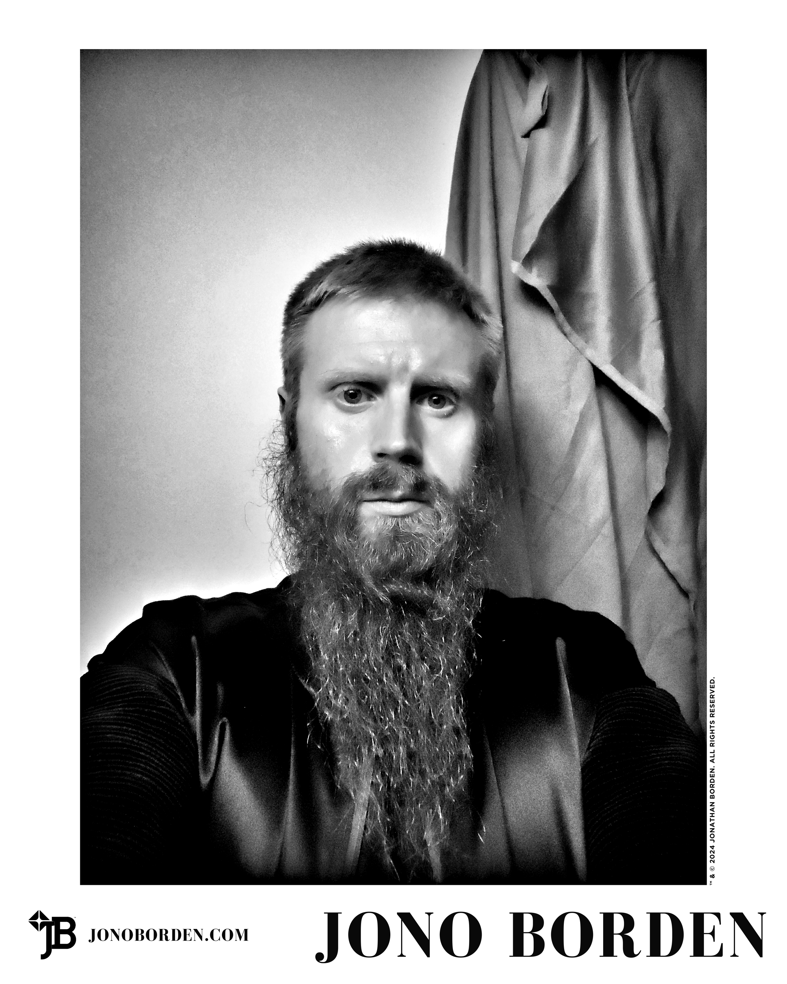 Black-and-white self-portrait of Jono Borden with large beard, seated in front of drapery, wearing a satin jacket, glaring at the viewer head-on, with a grave expression, imitating the pose of John Dee, the famous Elizabethan magician, taken in 2020.