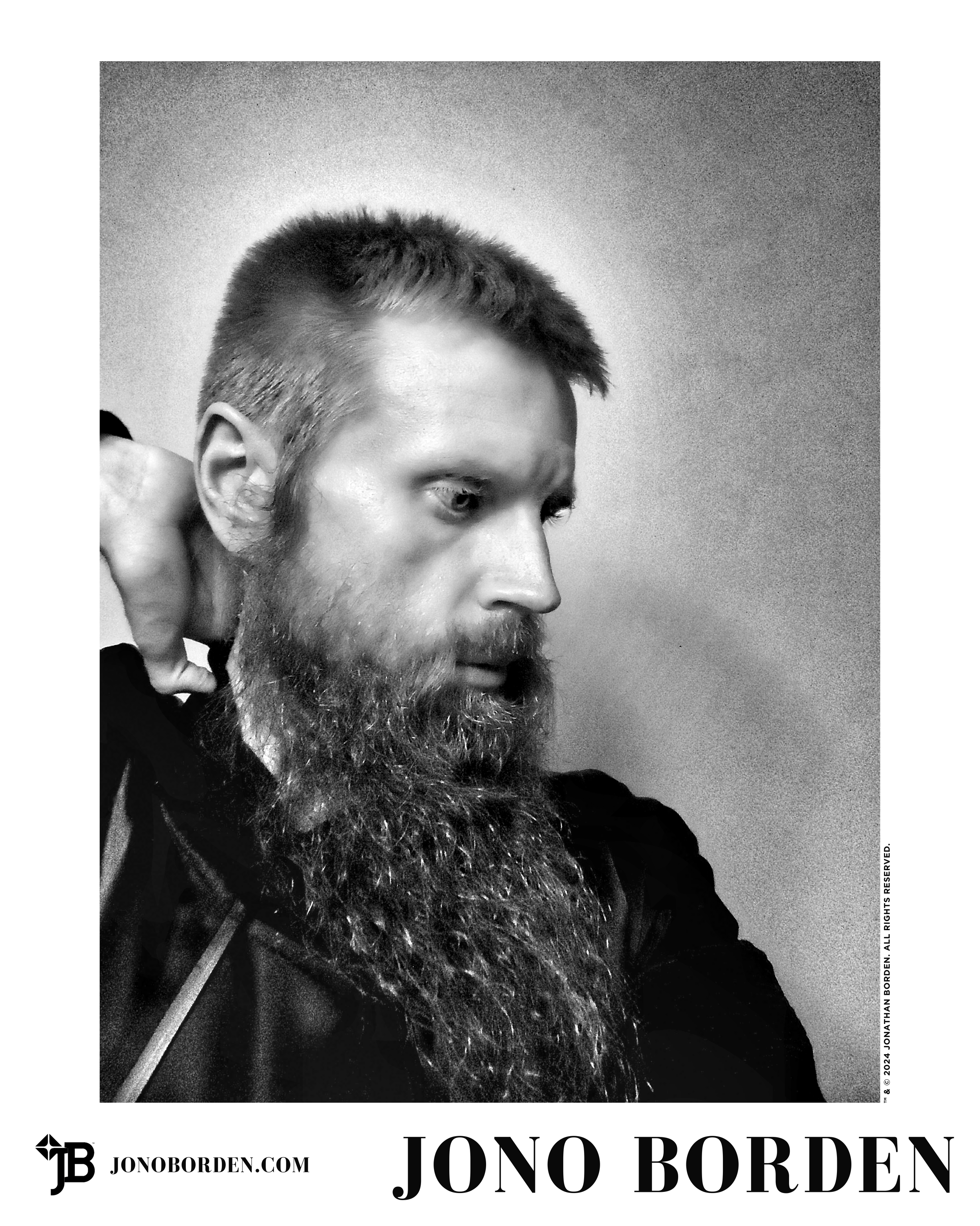Black-and-white self-portrait of Jono Borden looking to the right of the frame, his right hand behind his head and satin jacket open, with a long beard and solemn expression, taken of himself in 2020.