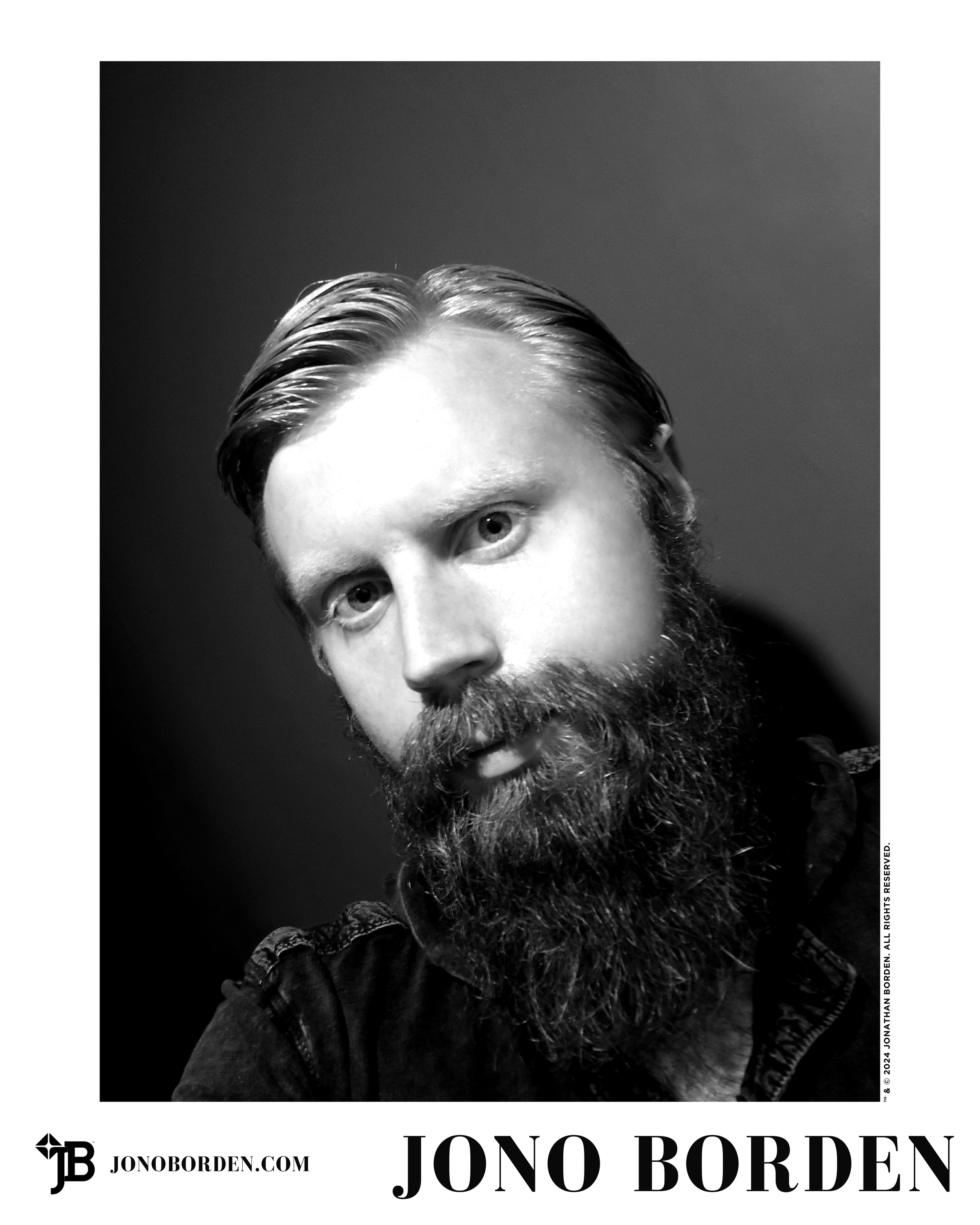 Black-and-white self-portrait of Jono Borden facing the viewer, close-up, centre of frame, hair styled and parted, beard trimmed, glaring at the viewer head-on with intense eyes, wearing a black shirt, taken of himself in 2015.