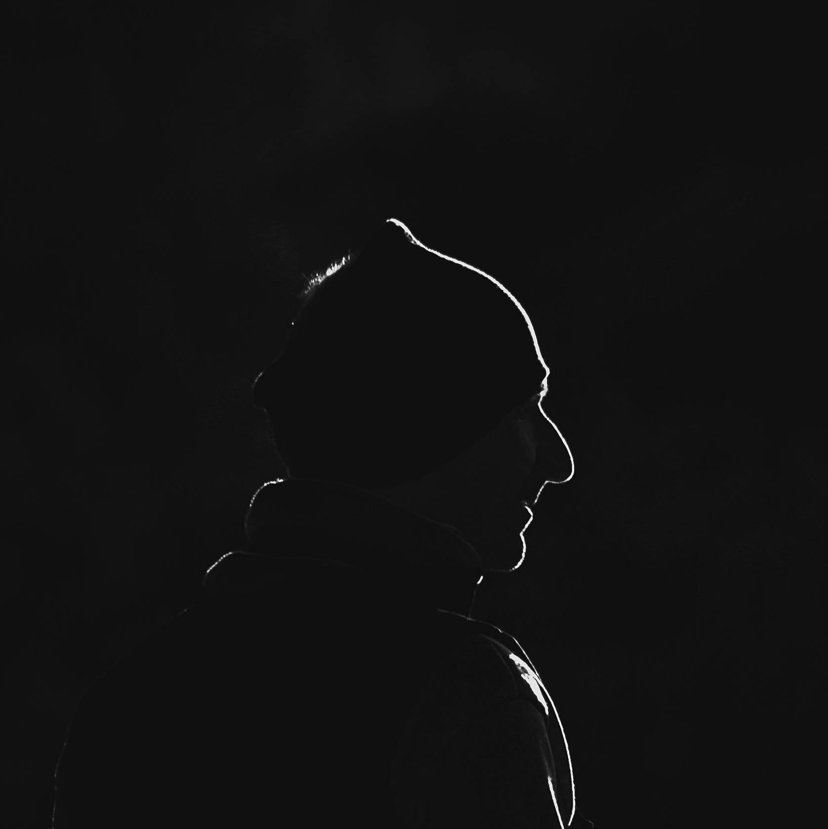 Silhouette of a person wearing a beanie and hoodie against the dark background.