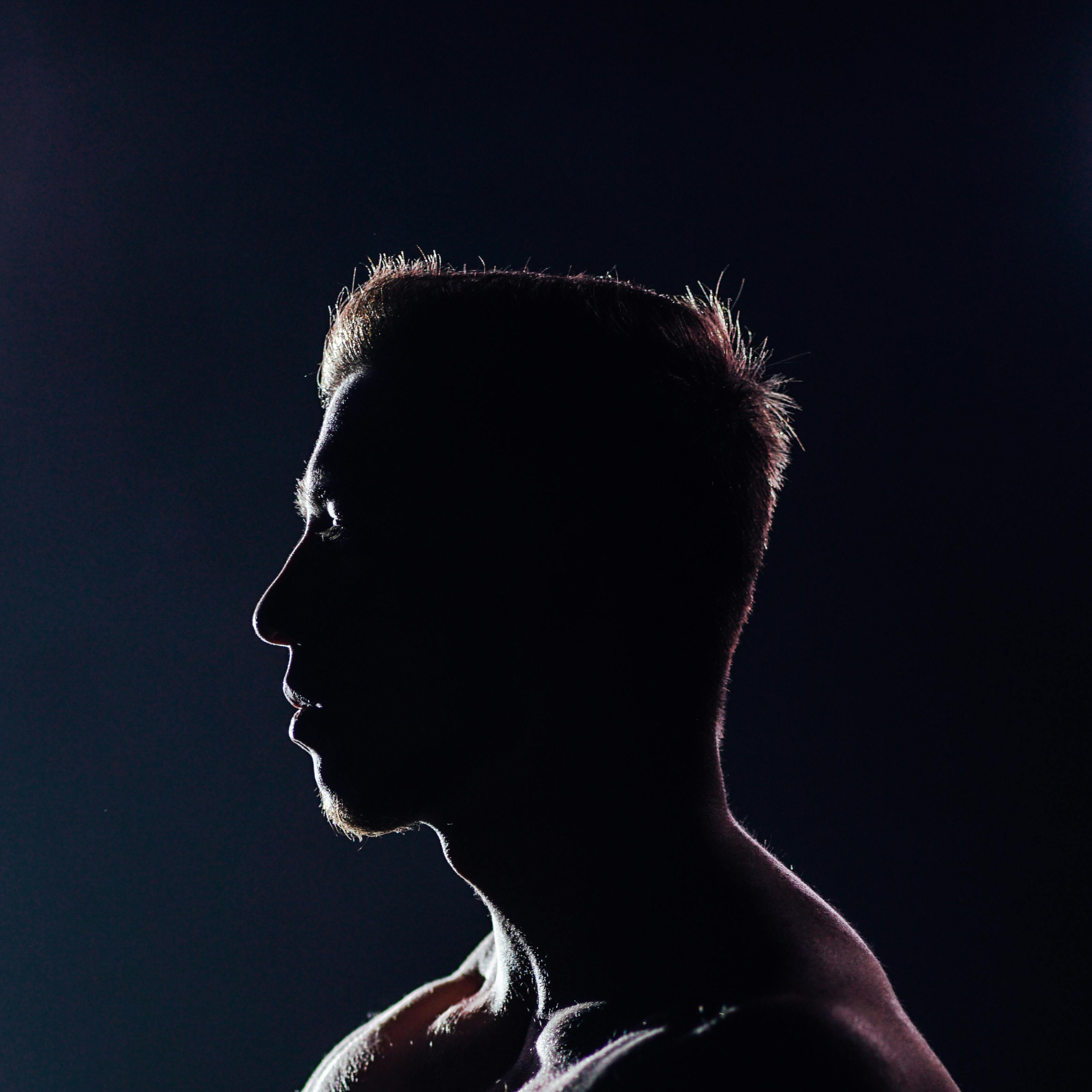 Silhouette of a person with short hair against a dark background, illuminated from behind creating a glowing outline.