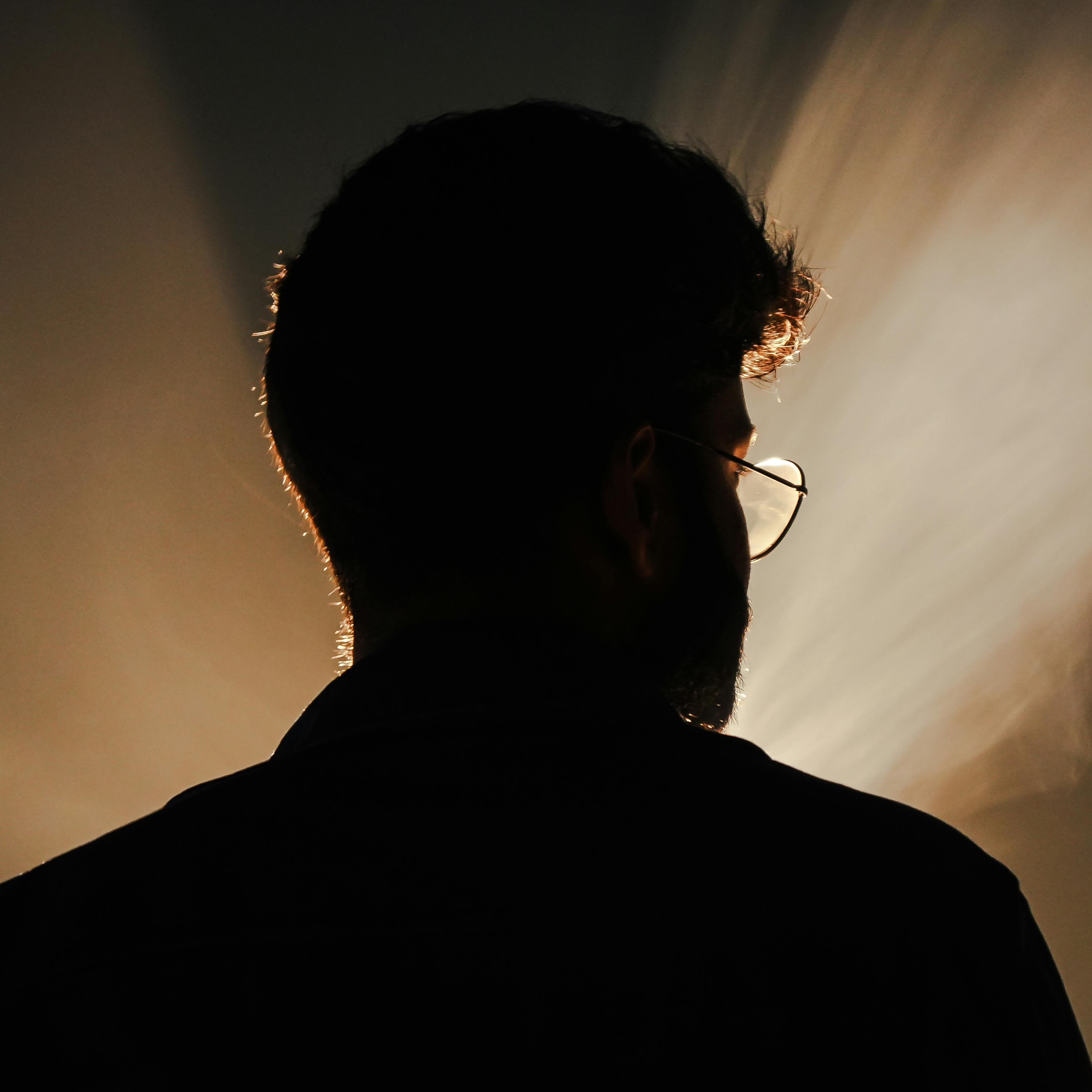 Silhouette of a man with glasses, backlit by a soft light creating a halo effect around his head and shoulders.