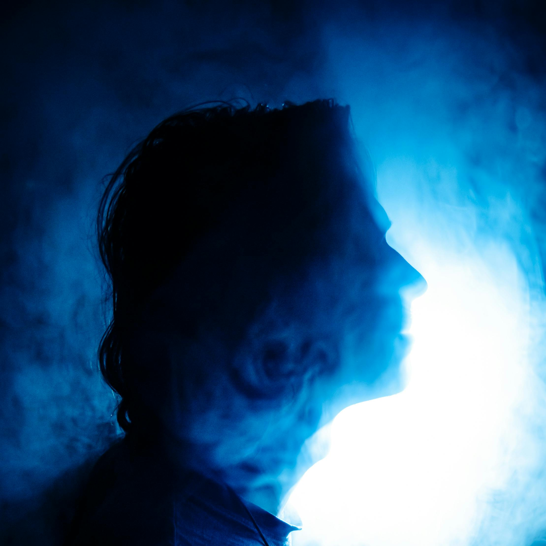 Silhouette of a person's profile with blue backlight and mist or smoke surrounding them.