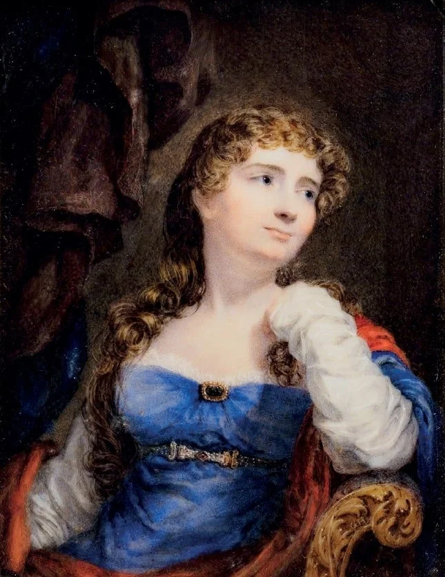 A young woman with long, curly brown hair in historical clothing, sitting in a decorated chair with a contemplative expression, with a dark background.
