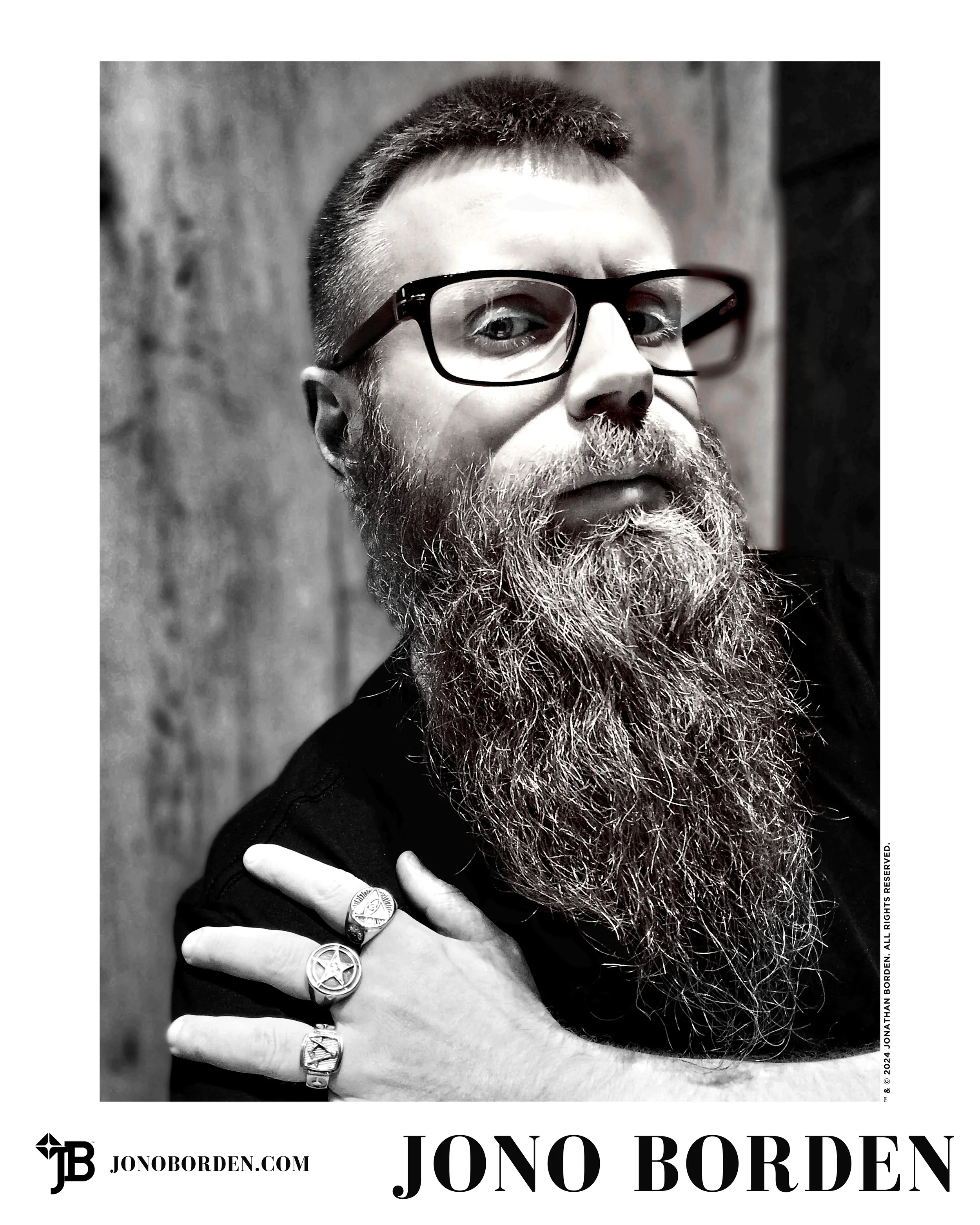 Black-and-white self-portrait of Jono Borden turned to face the camera, his left hand with many large silver rings resting on his right shoulder, taken of himself in 2024.