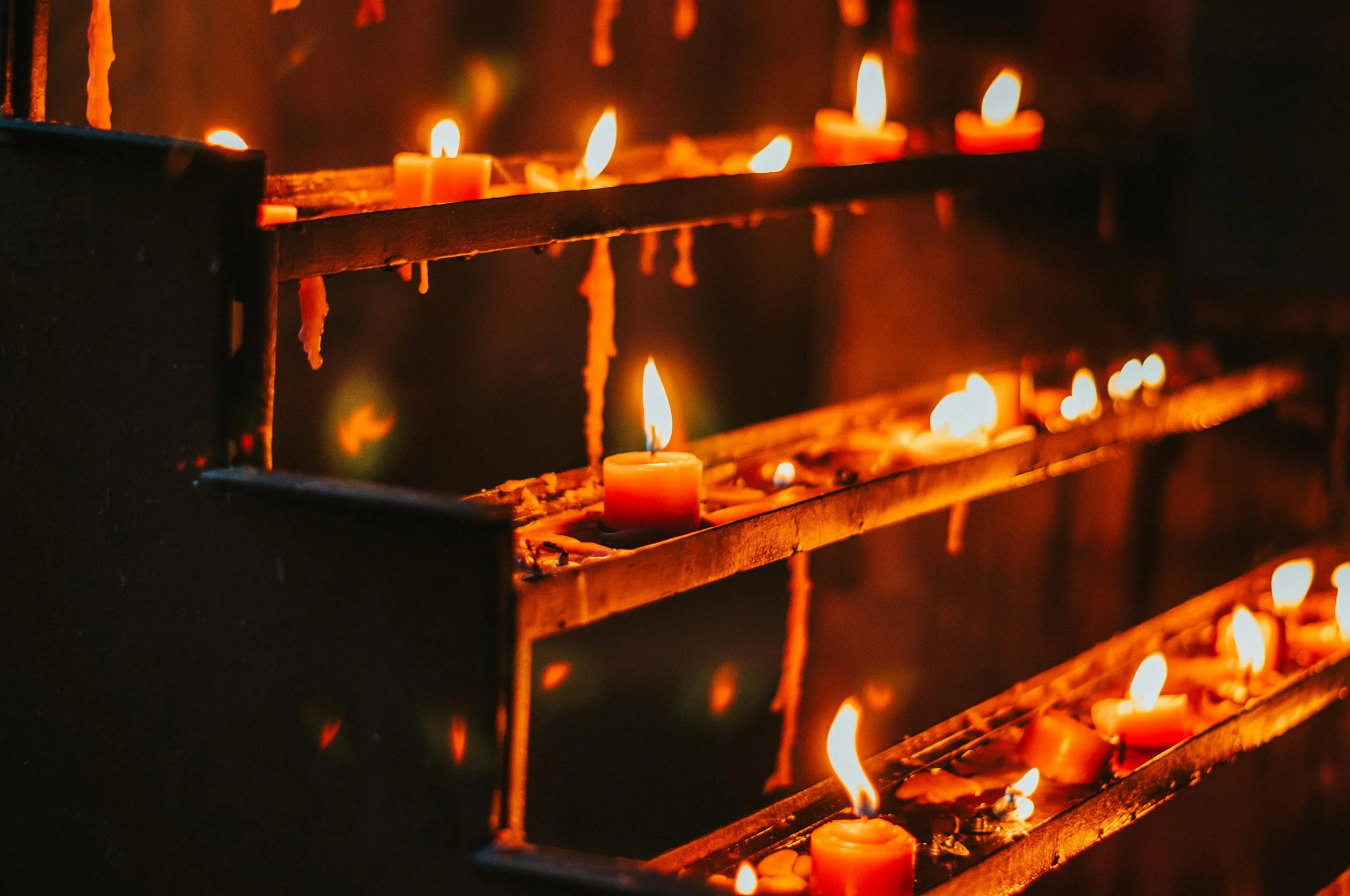 Multiple candles burning on a metal shelf, creating a warm glow with melting wax drippings.