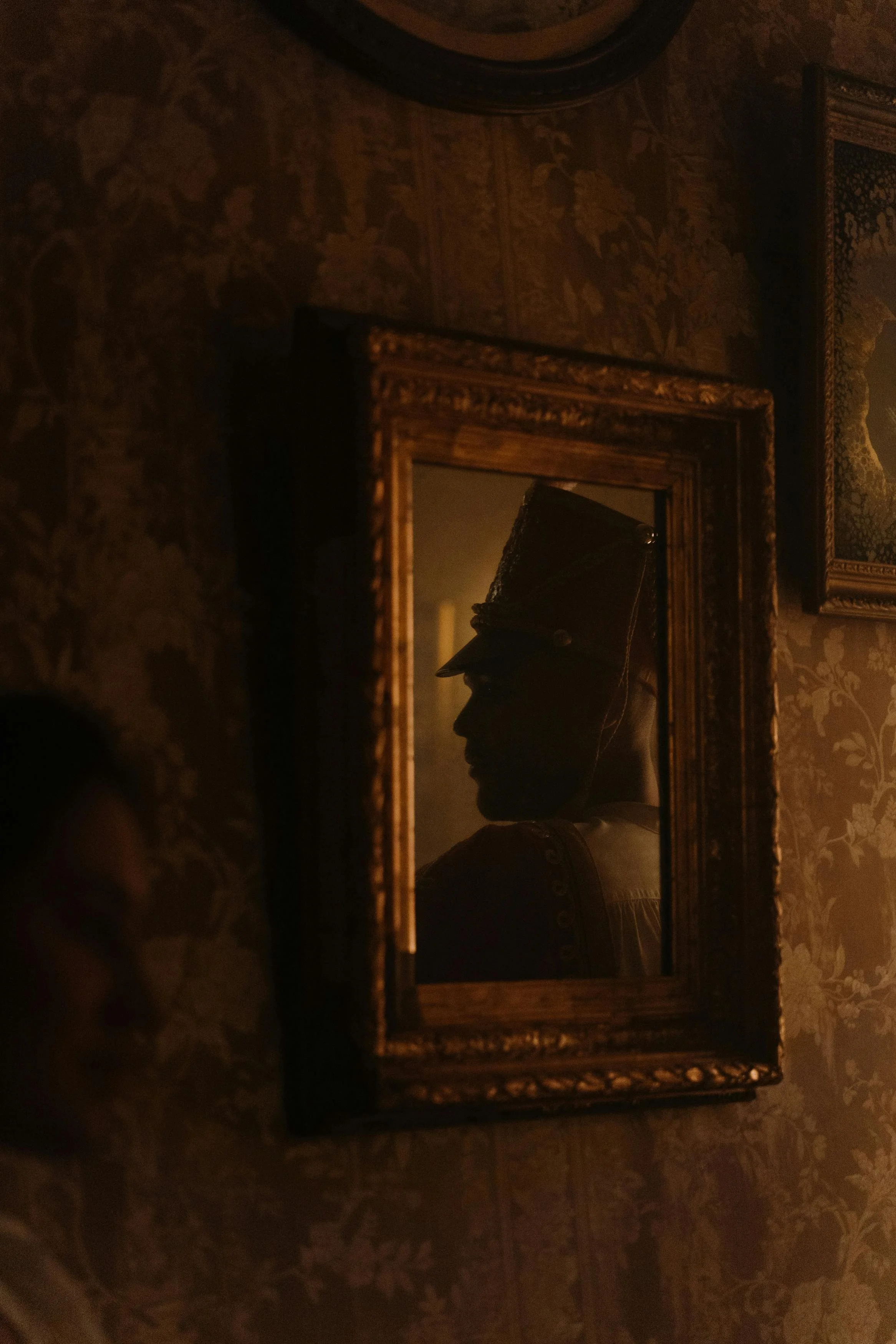 A silhouette of a person dressed as a soldier, viewed through an ornate framed mirror on a decorative wall.