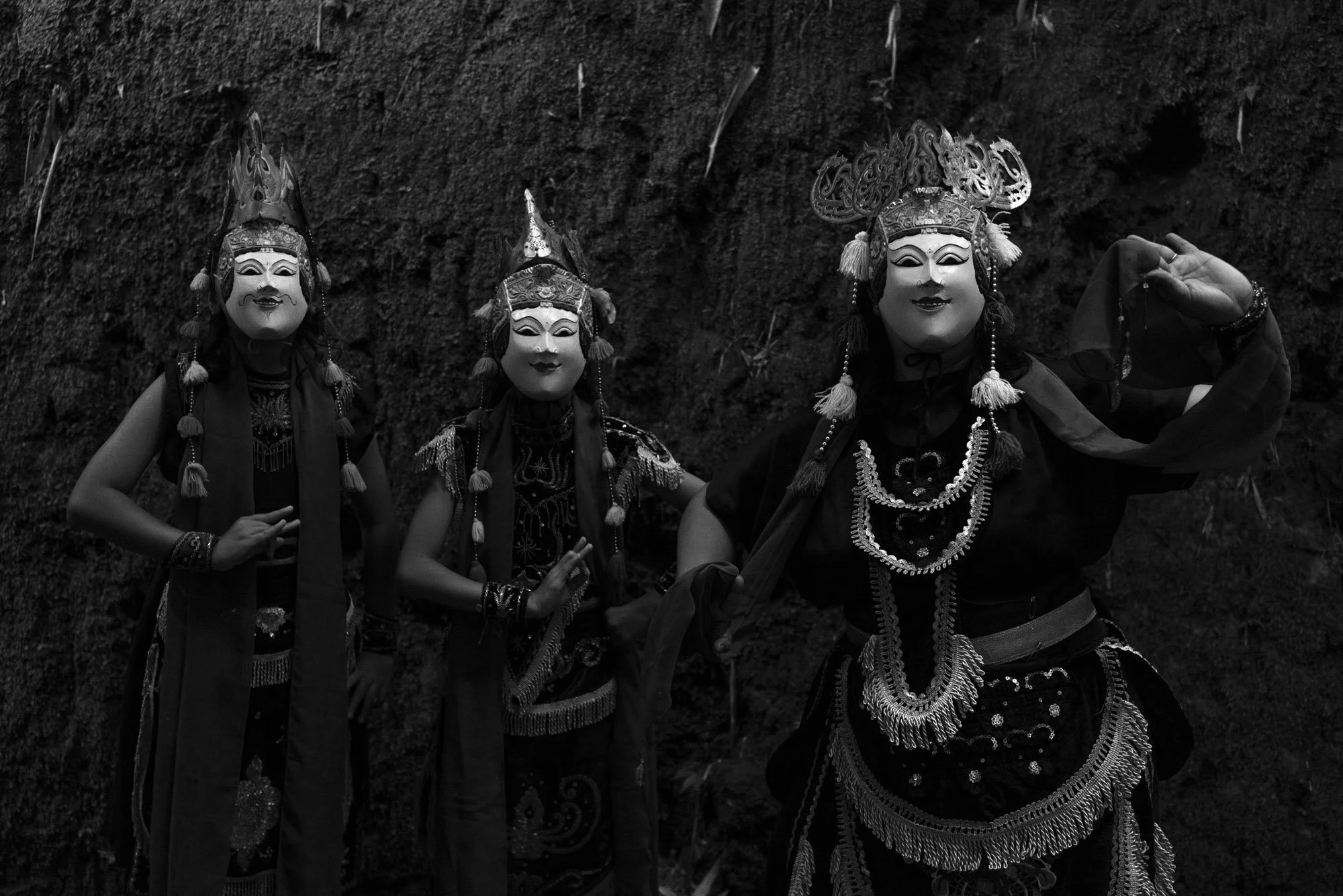 Three Topeng malang performers dressed in traditional attire with Topeng masks and headdresses, standing against a textured wall.