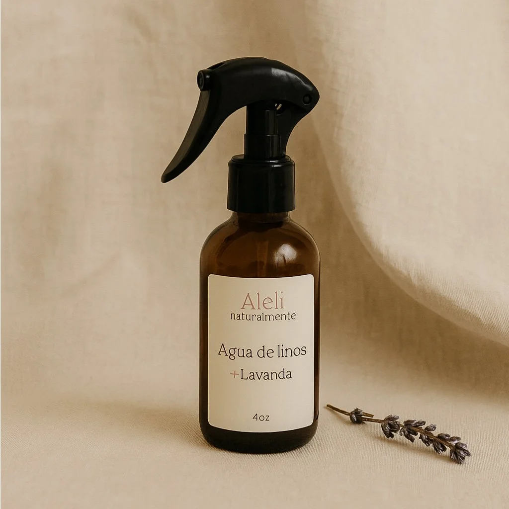 Frasco de spray con etiqueta que dice 'Aleli naturalmente agua de linos + lavanda 4oz', junto a una ramita de lavanda sobre fondo beige.