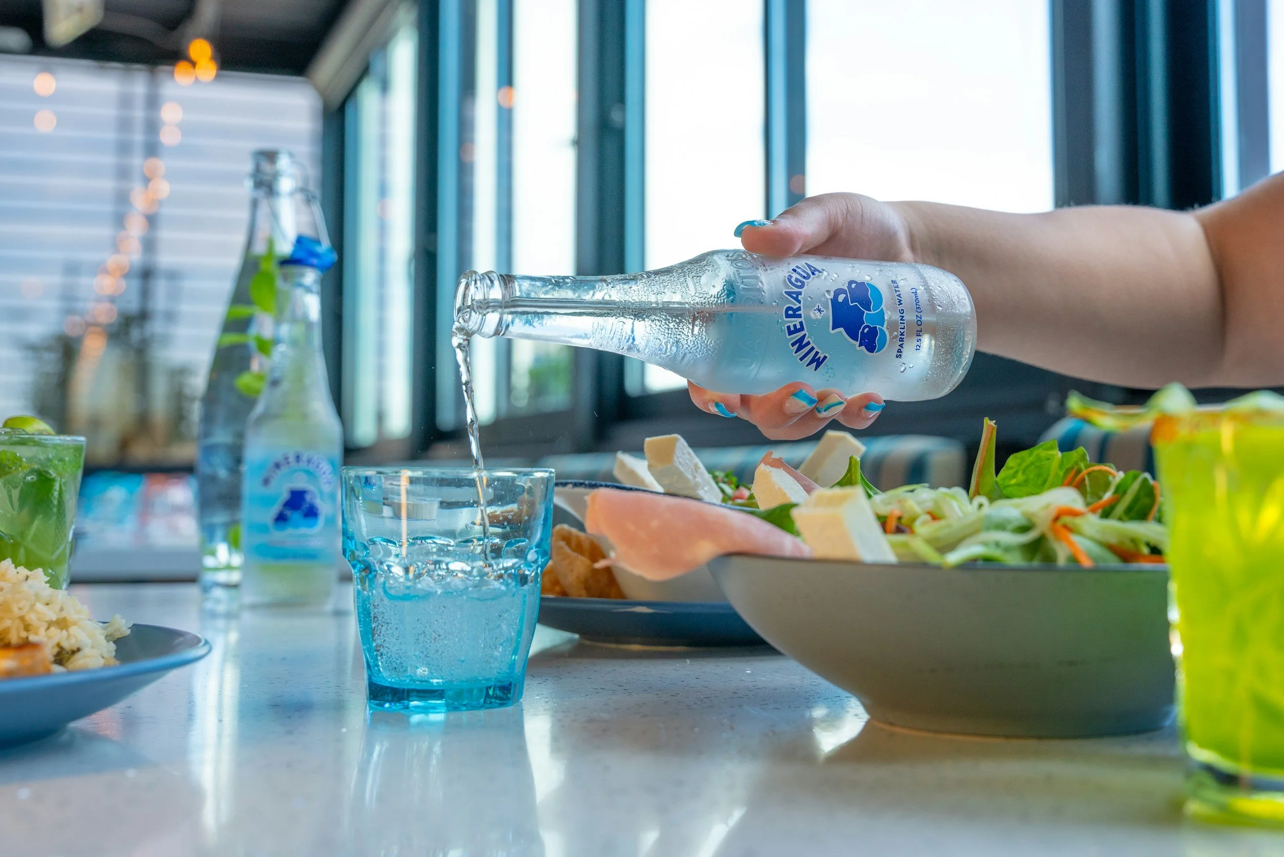 water being pourd into a glass on a table next to a healthy salad bowl