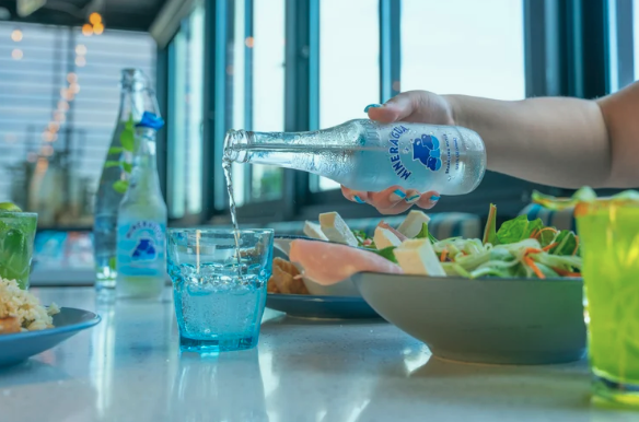 pouring water into a glass next to a healthy salad bowl