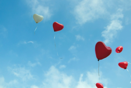 Sky with blue clouds and red and white heart-shaped balloons floating.