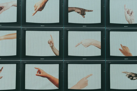 Nine television screens displaying various human hands pointing in different directions.