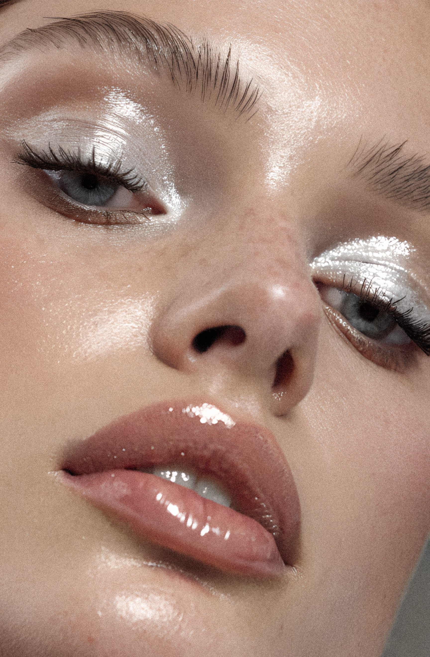 Close-up of a woman's face with glossy lips, shimmering eye makeup, and well-groomed eyebrows.