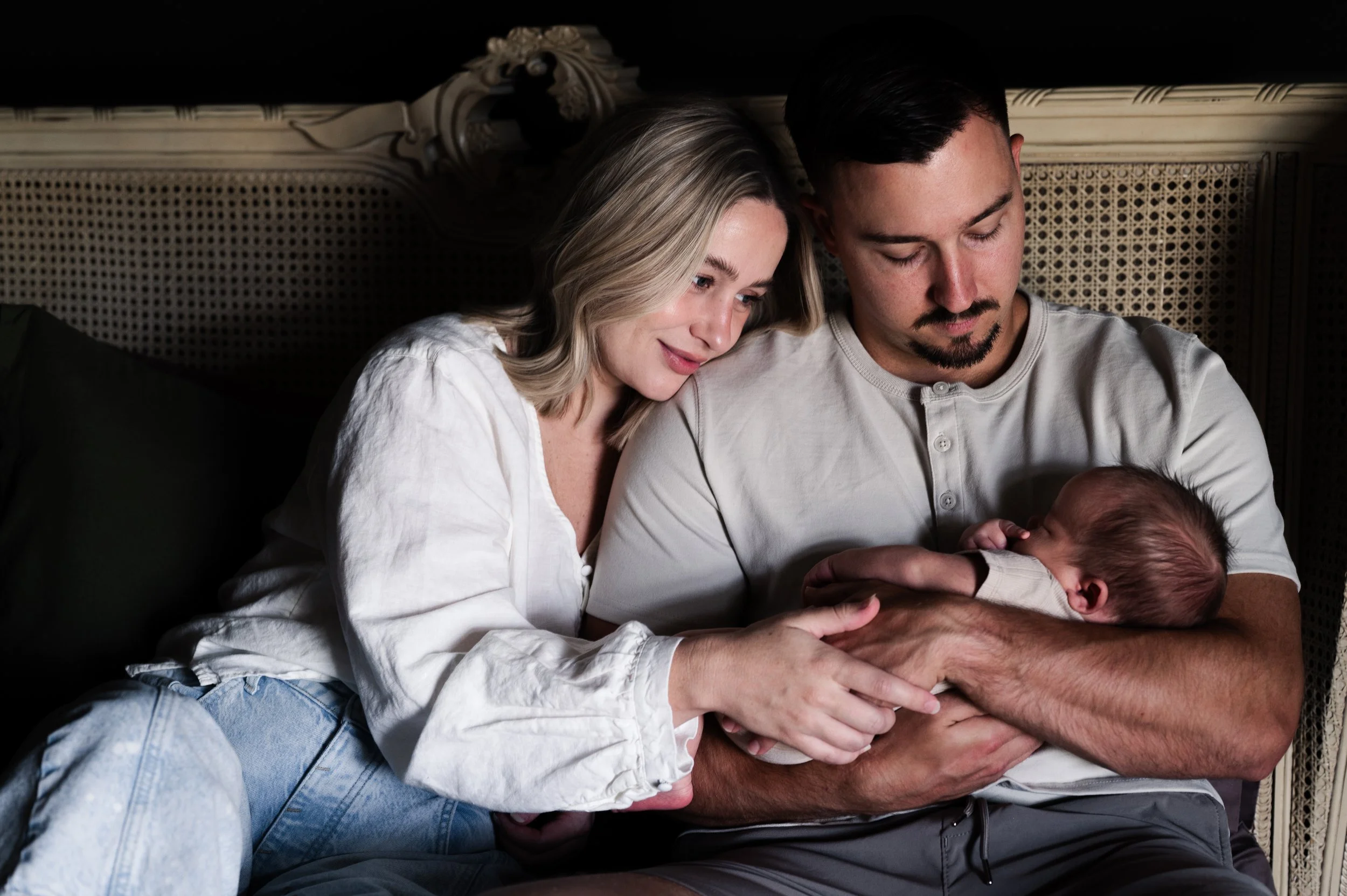 blonde woman and dark haired man sit on bed with rattan headboard cradling sleeping newborn baby in clarksville, tennessee