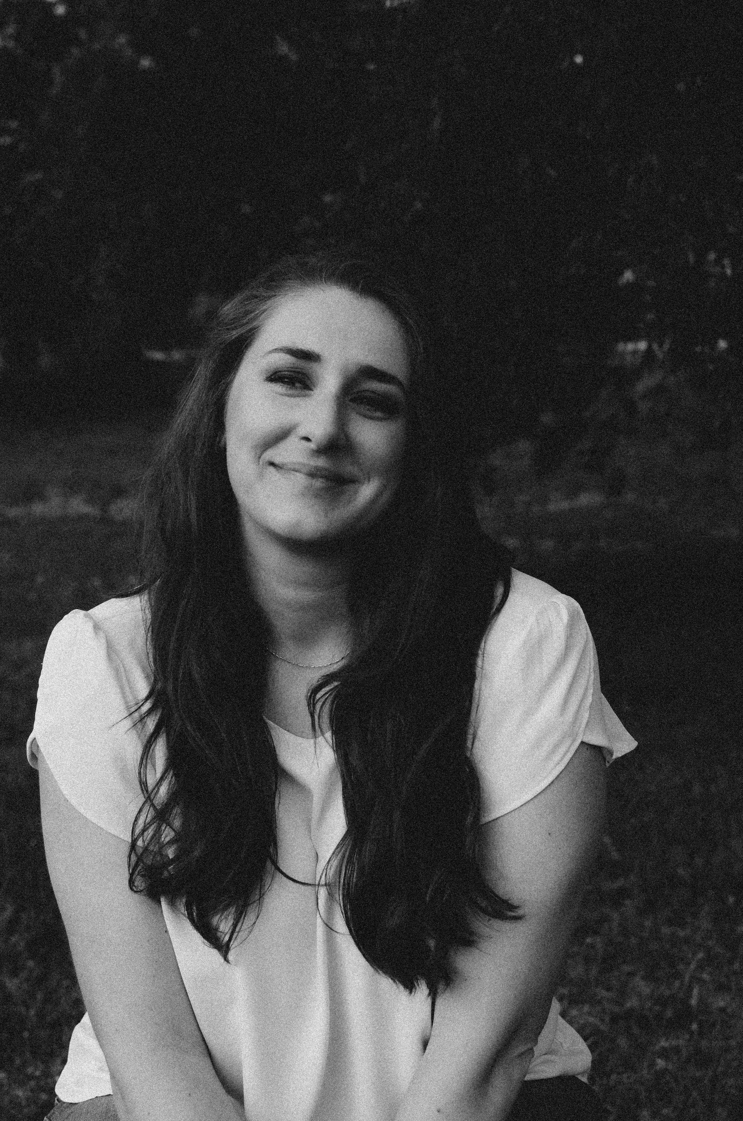 A smiling woman with long dark hair sitting outdoors near at golden hour sunset