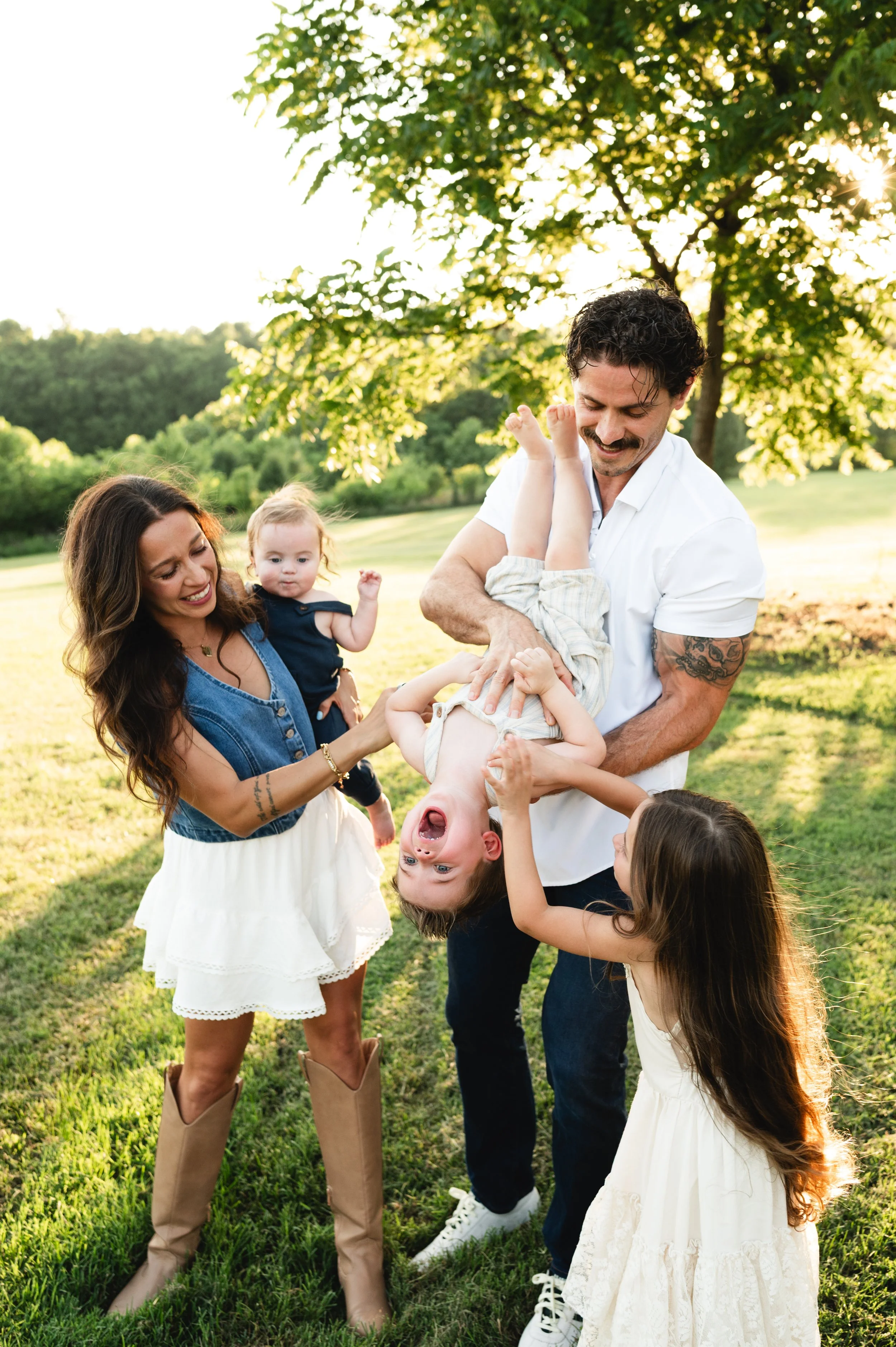 a young family of five plays in grassy field with trees during sunny summer sunset in Clarksville, Tennessee.