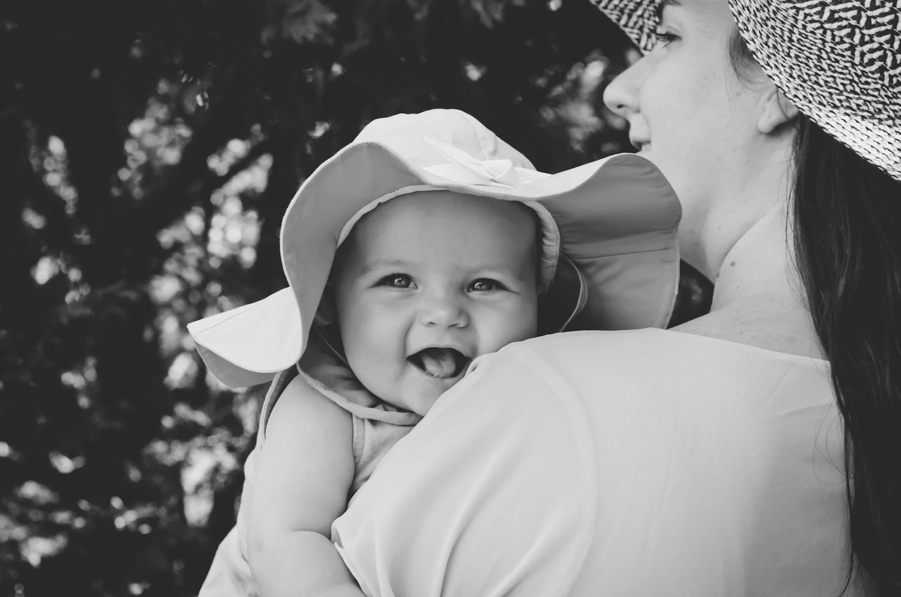 black and white photo of smiling baby wearing hat looking over mother's shoulder, clarksville tn, nashville tn, photographer, motherhood, family, newborn, outdoor family photographer, affordable