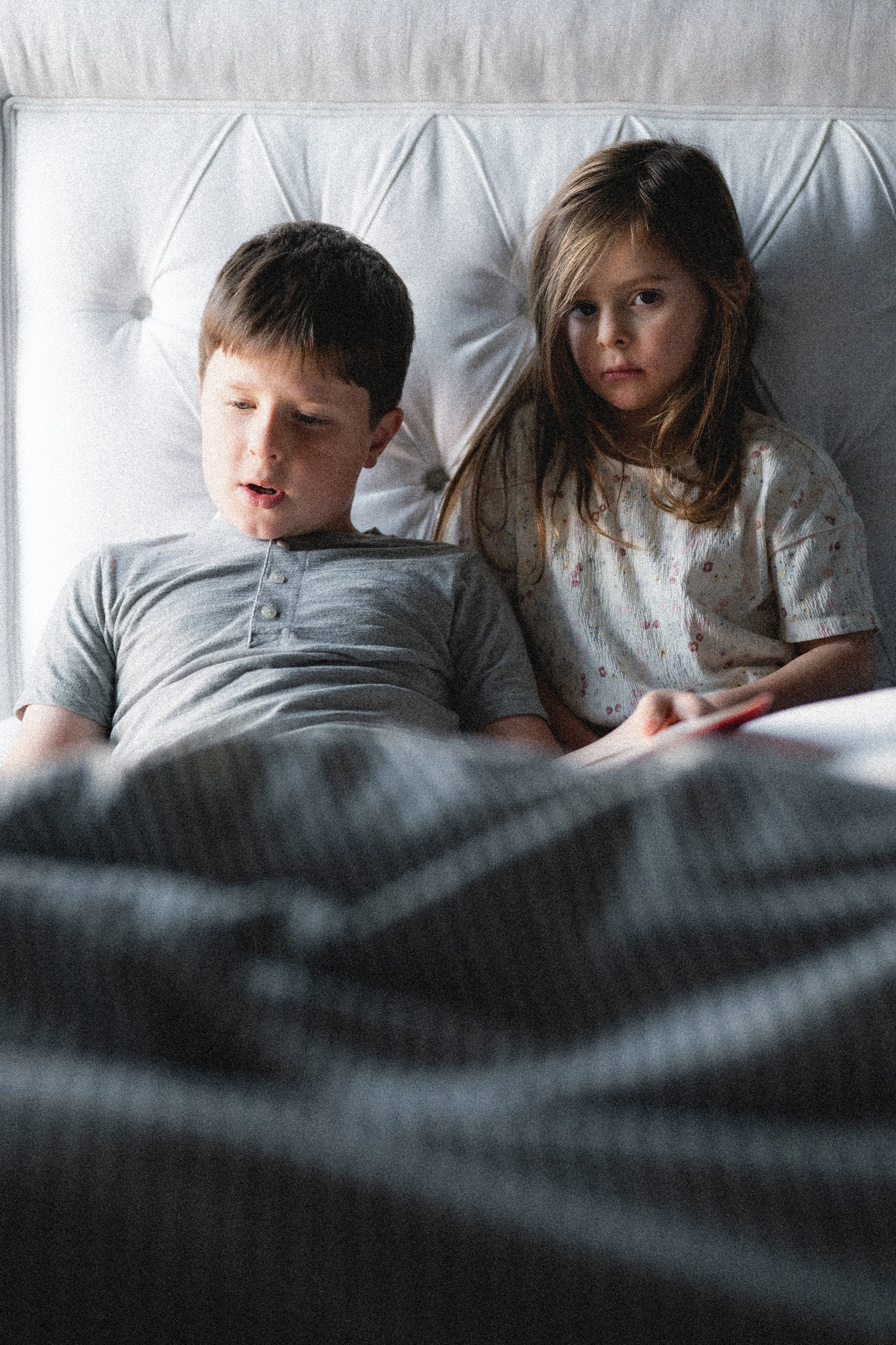 young boy in gray shirt leans against white headboard reading to younger brunette girl, photographer, clarksville tn, nashville tn, family photographer, lifestyle family photographer, affordable