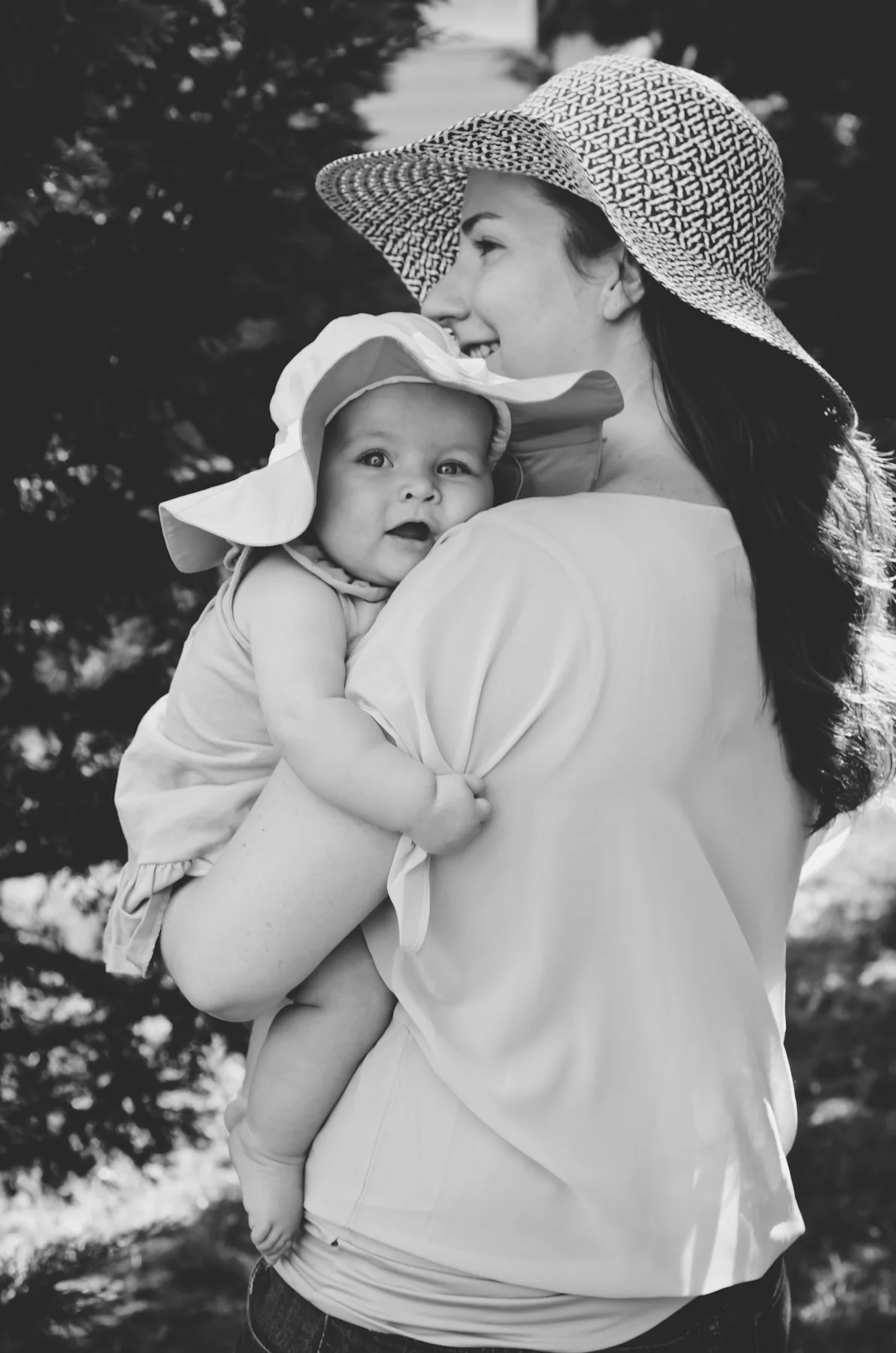 black and white photo of young mother holding baby girl wearing hat and resting on mother's shoulder, clarksville tn, nashville tn, photographer, motherhood, family photographer, film photographer, affordable
