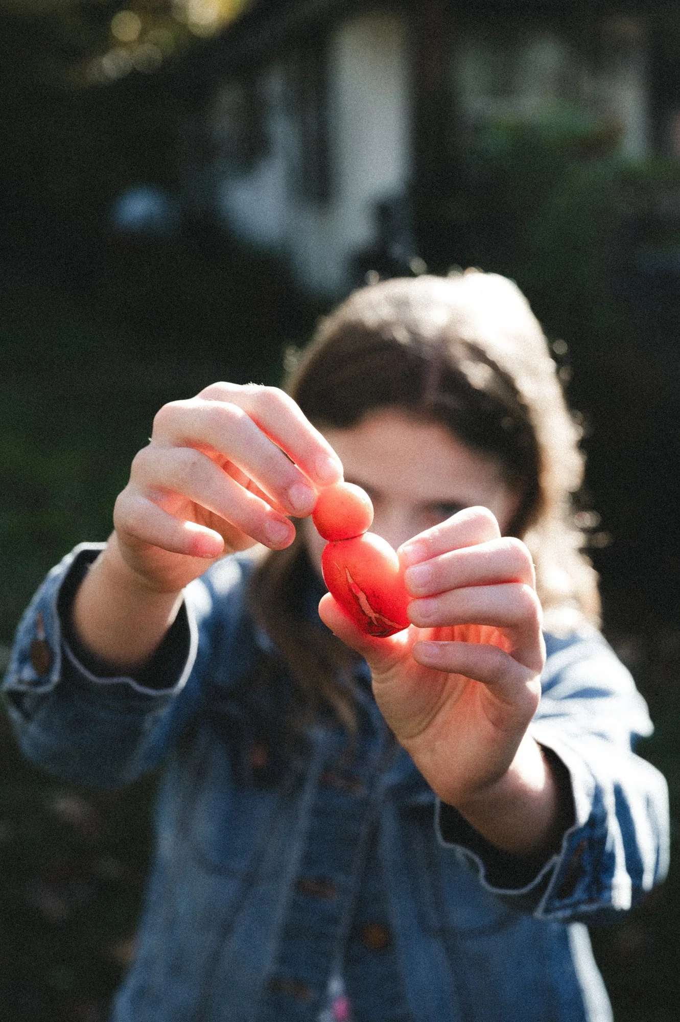 A person holding a red almond-shaped object with both hands, outdoors in natural light, with a blurred background.