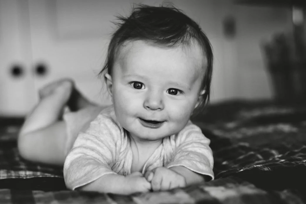 black and white photo of smiling newborn laying on bed in bedroom, clarksville tn, nashville tn, clarksville tennessee, nashville tennessee, affordable, photographer