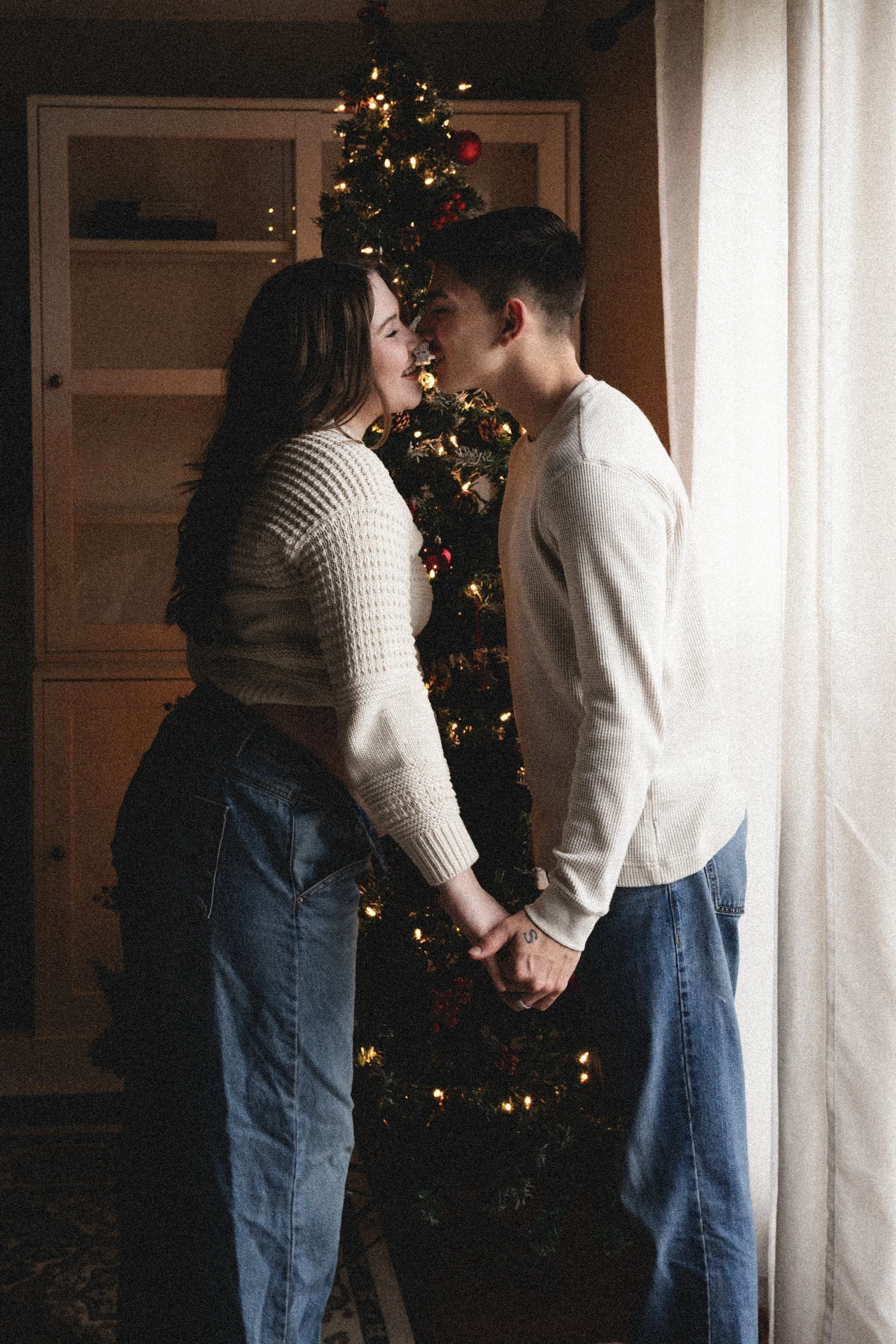 pregnant woman and husband stand kissing in front of christmas tree by window, clarksville tn, nashville tn, photographer, maternity photographer, newborn photographer, moody, affordable, neutral, bold, lifestyle