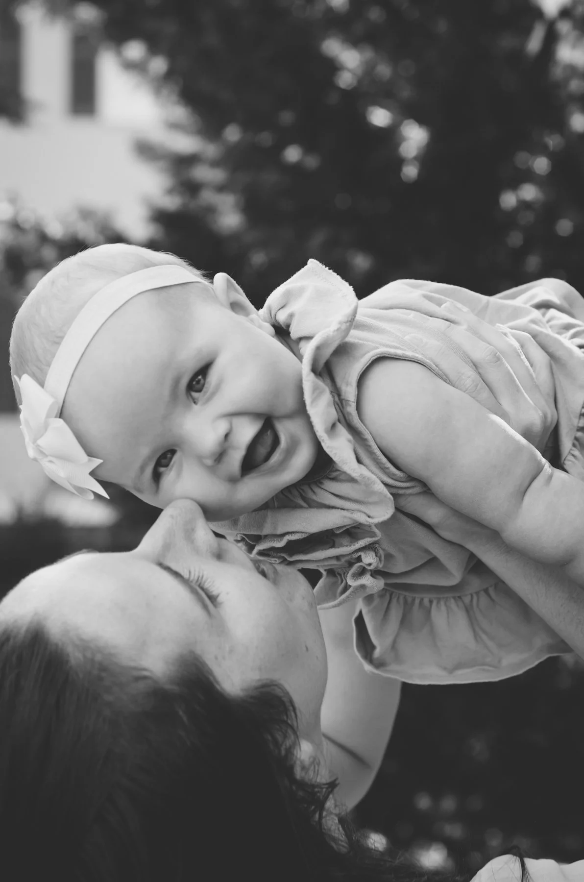 black and white photo of mother holding up smiling baby girl wearing headband for outdoor family photoshoot, photographer, affordable, family photographer, clarksville tn, nashville tn