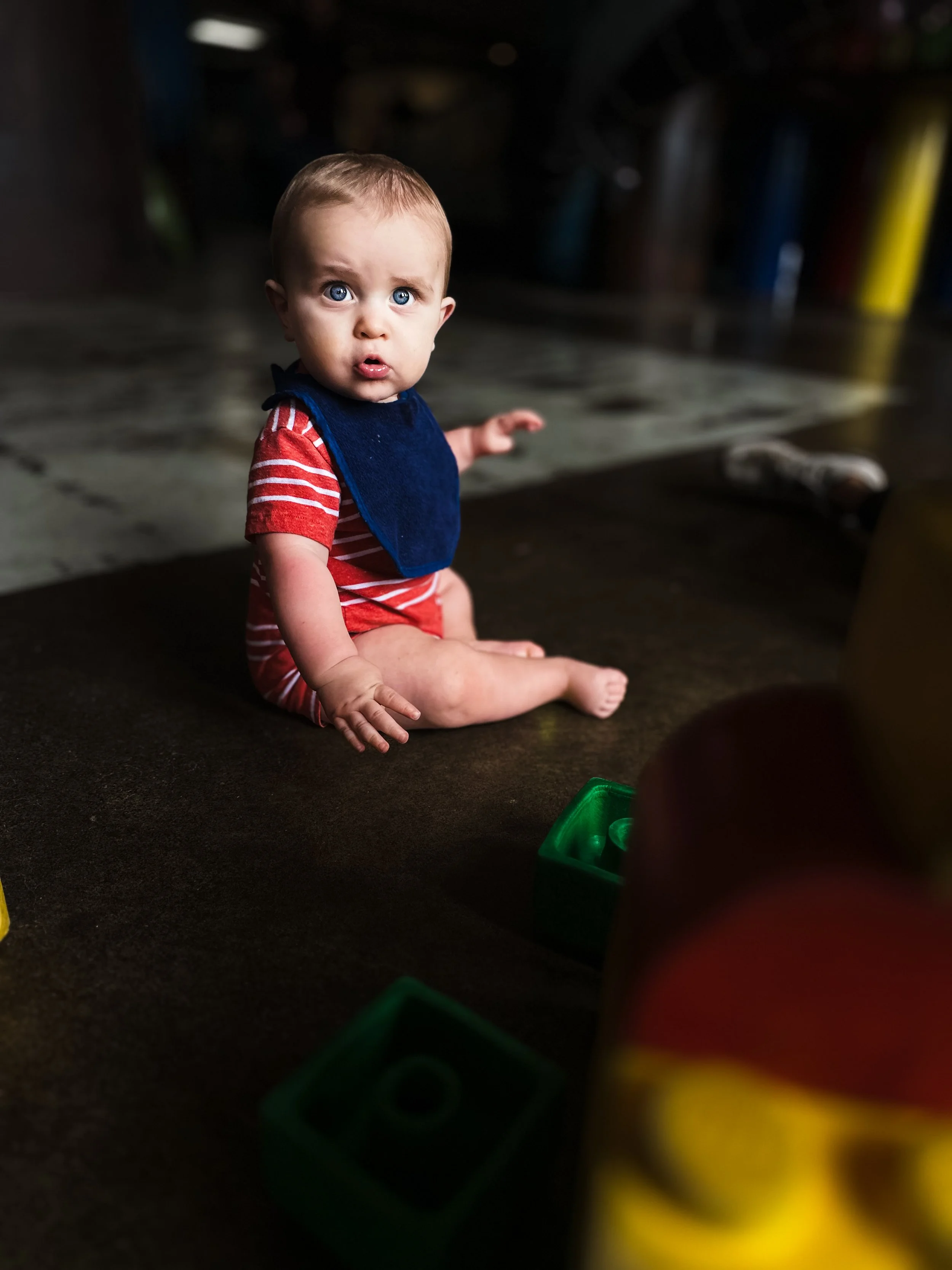 boy wearing red and white striped outfit with navy blue bib sits on concrete floor surrounded by colored blocks, family photographer, affordable, clarksville tennessee, nashville tennessee