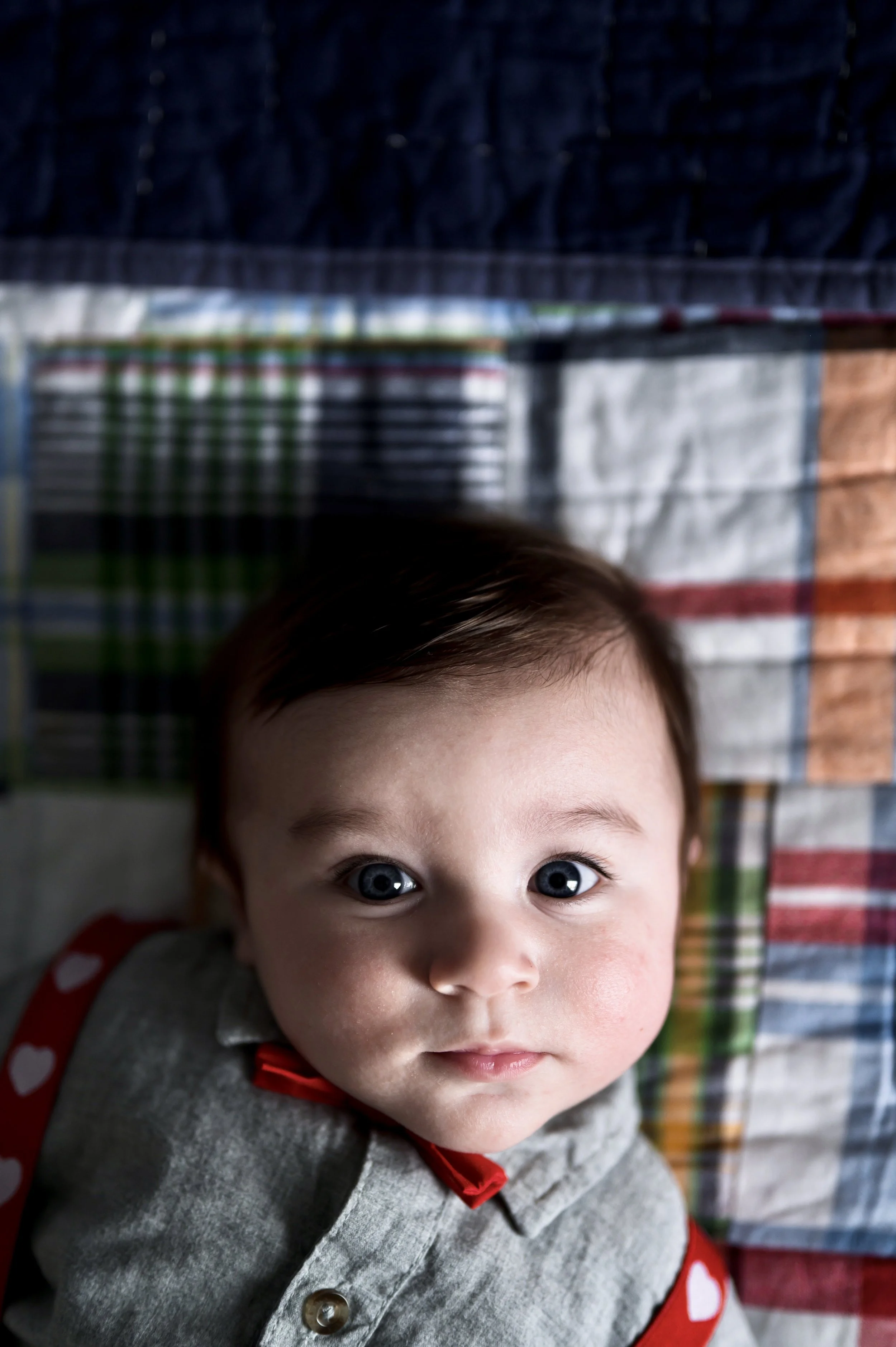 three month old baby boy with brown hair wearing red suspenders and bow tie lies on plaid blanket, clarksville tennessee photographer, nashville tennessee photographer, newborn photographer, milestone photographer, affordable
