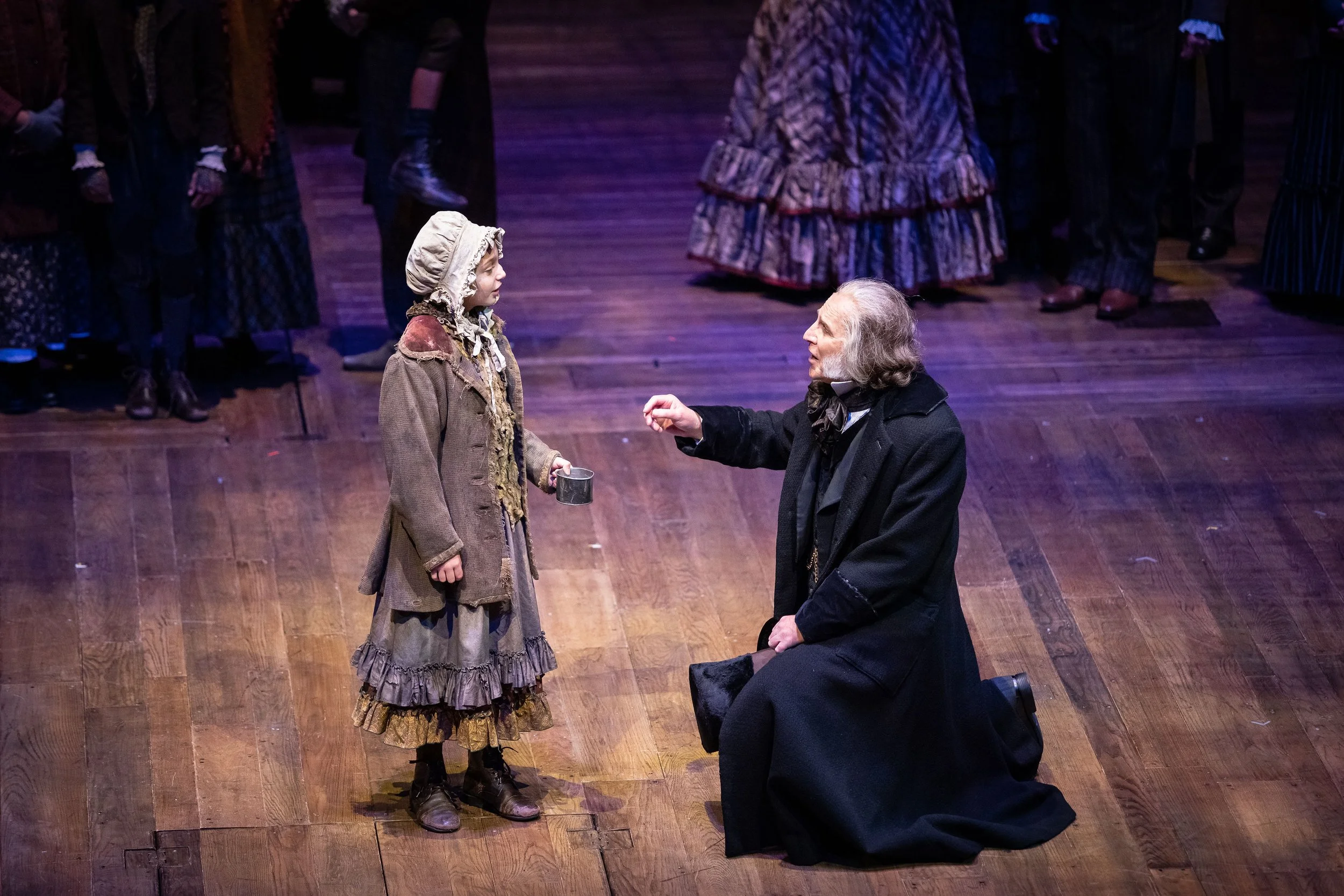 A theatrical scene from A Christmas Carol at The Denver Center for the Performing Arts with Beggar Child and Ebenezer Scrooge placing money in tin cup